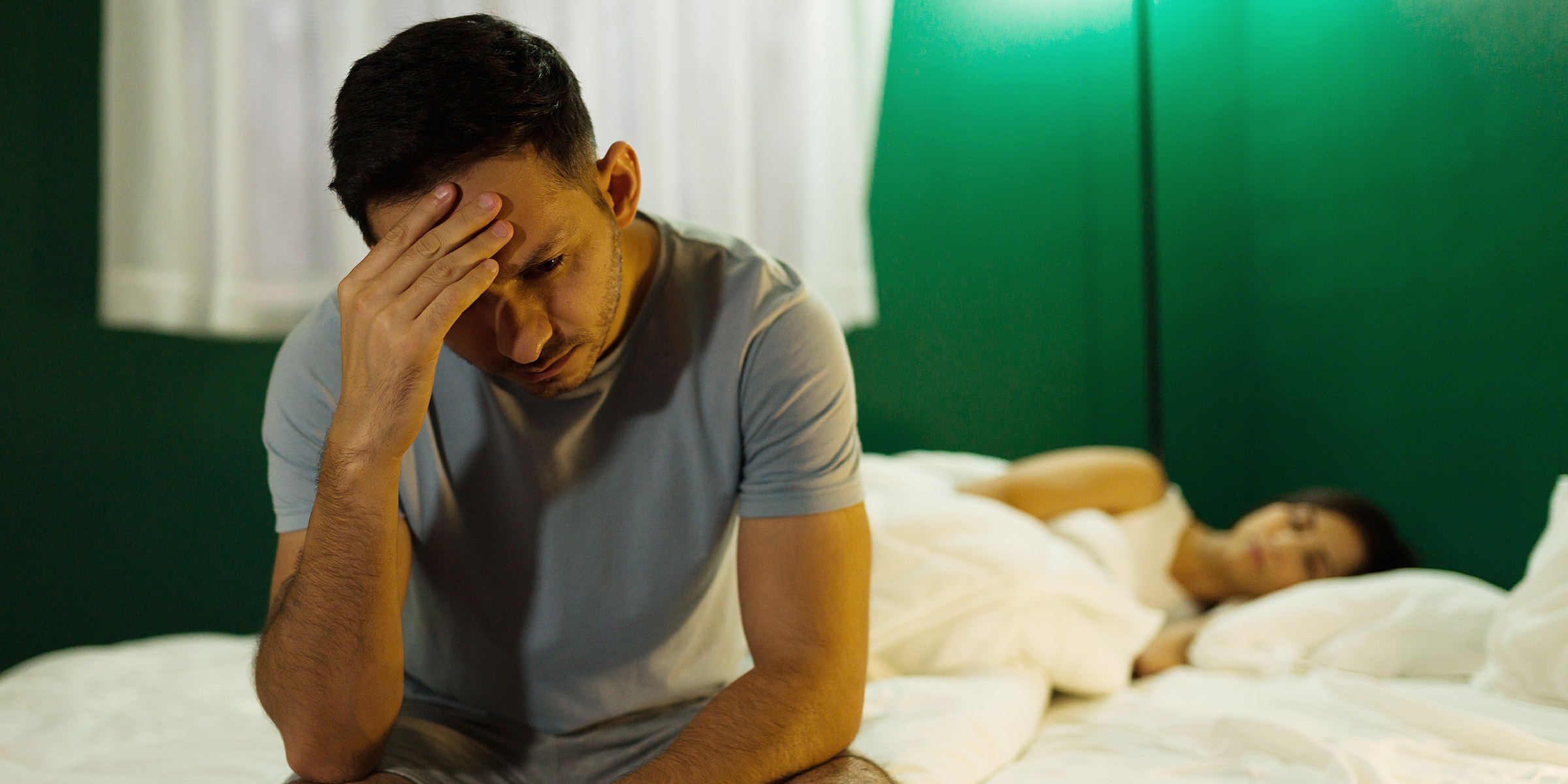 Un marido estresado sentado en la cama mientras su mujer duerme | Fuente: Shutterstock