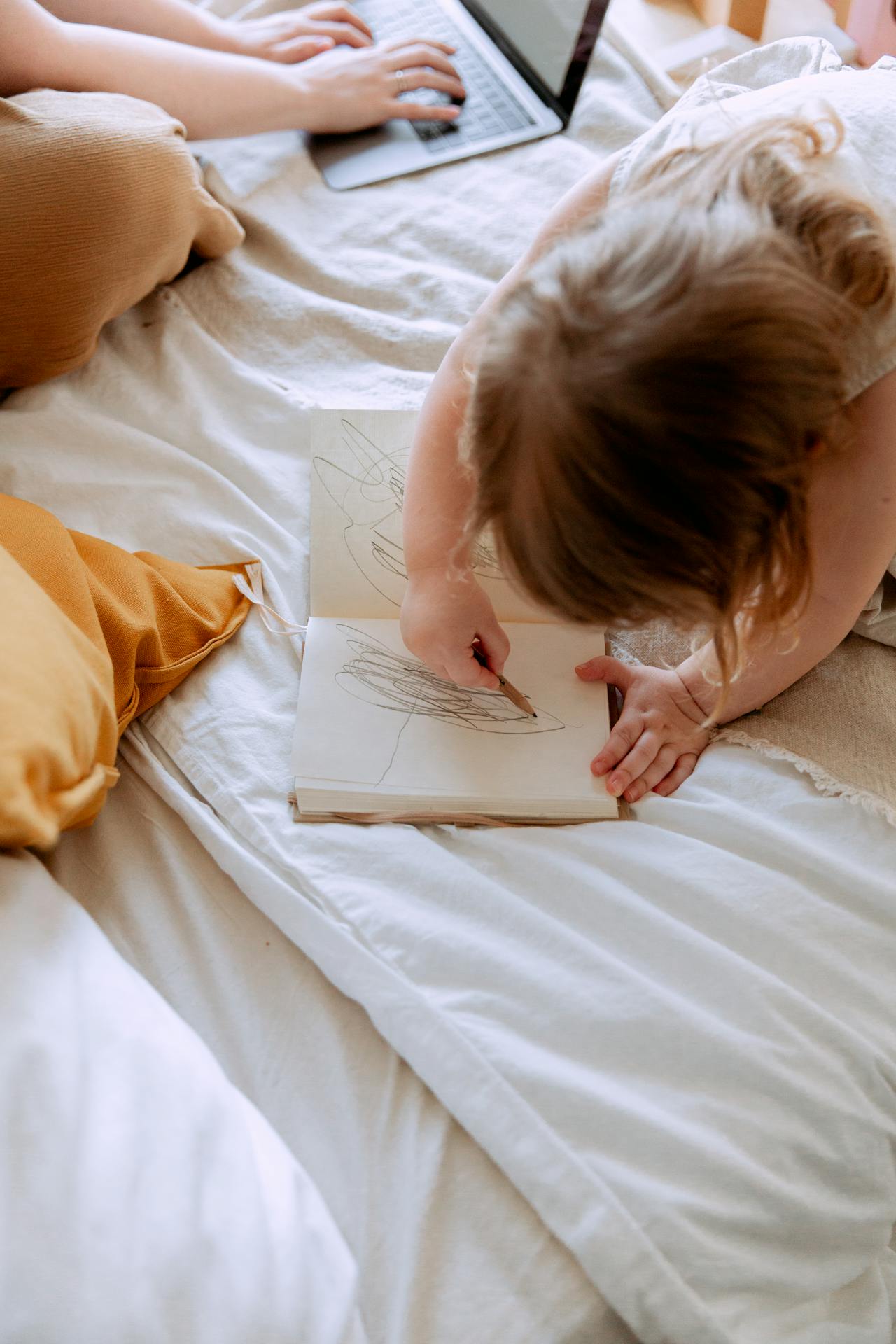 Mujer trabajando en su portátil mientras su hija pequeña garabatea en un cuaderno | Fuente: Pexels