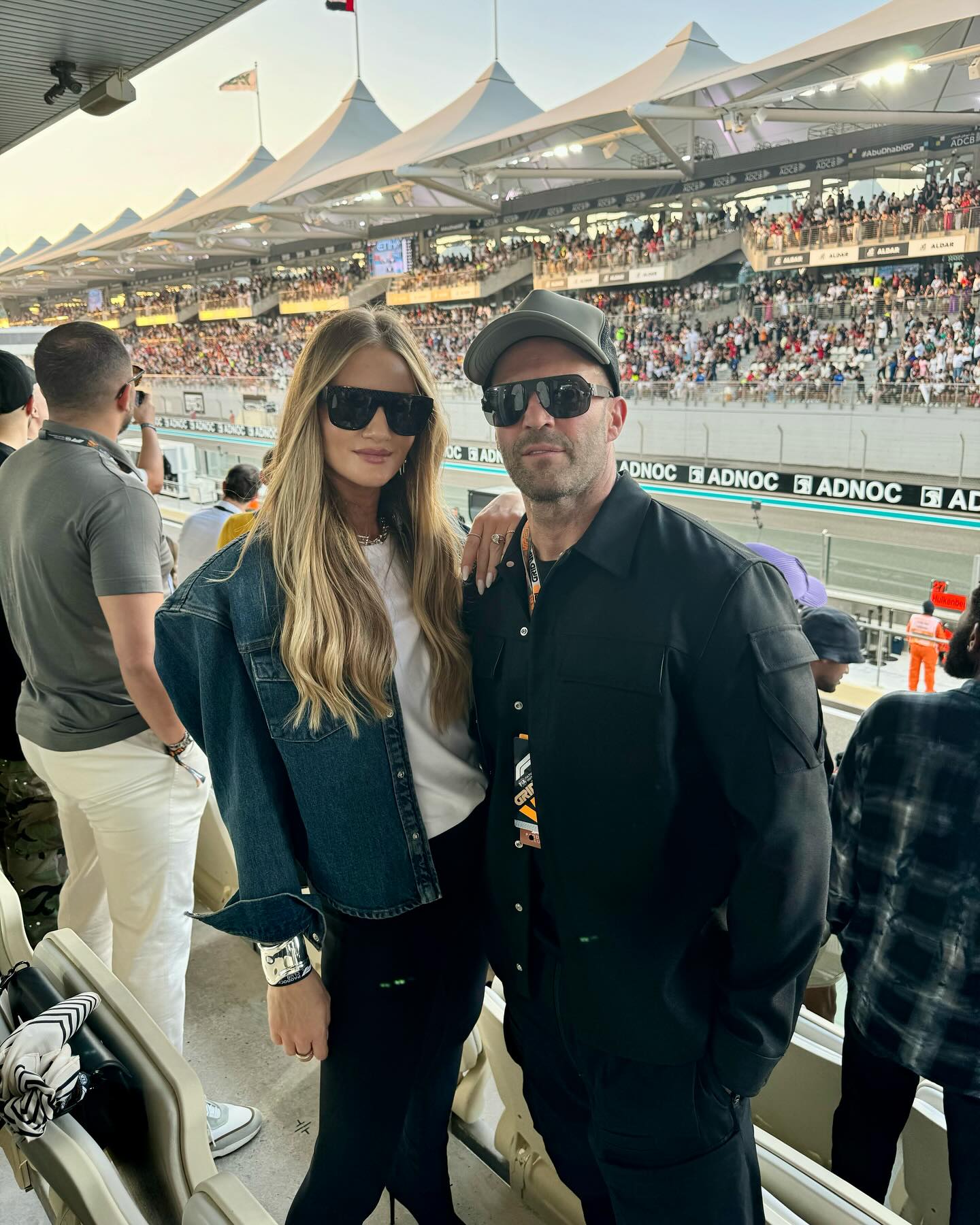 Rosie Huntington-Whiteley y Jason Statham posan a pie de pista en un evento automovilístico repleto de gente, ambos con gafas de sol oscuras y looks de lo más cool. | Fuente: Instagram/rosiehw
