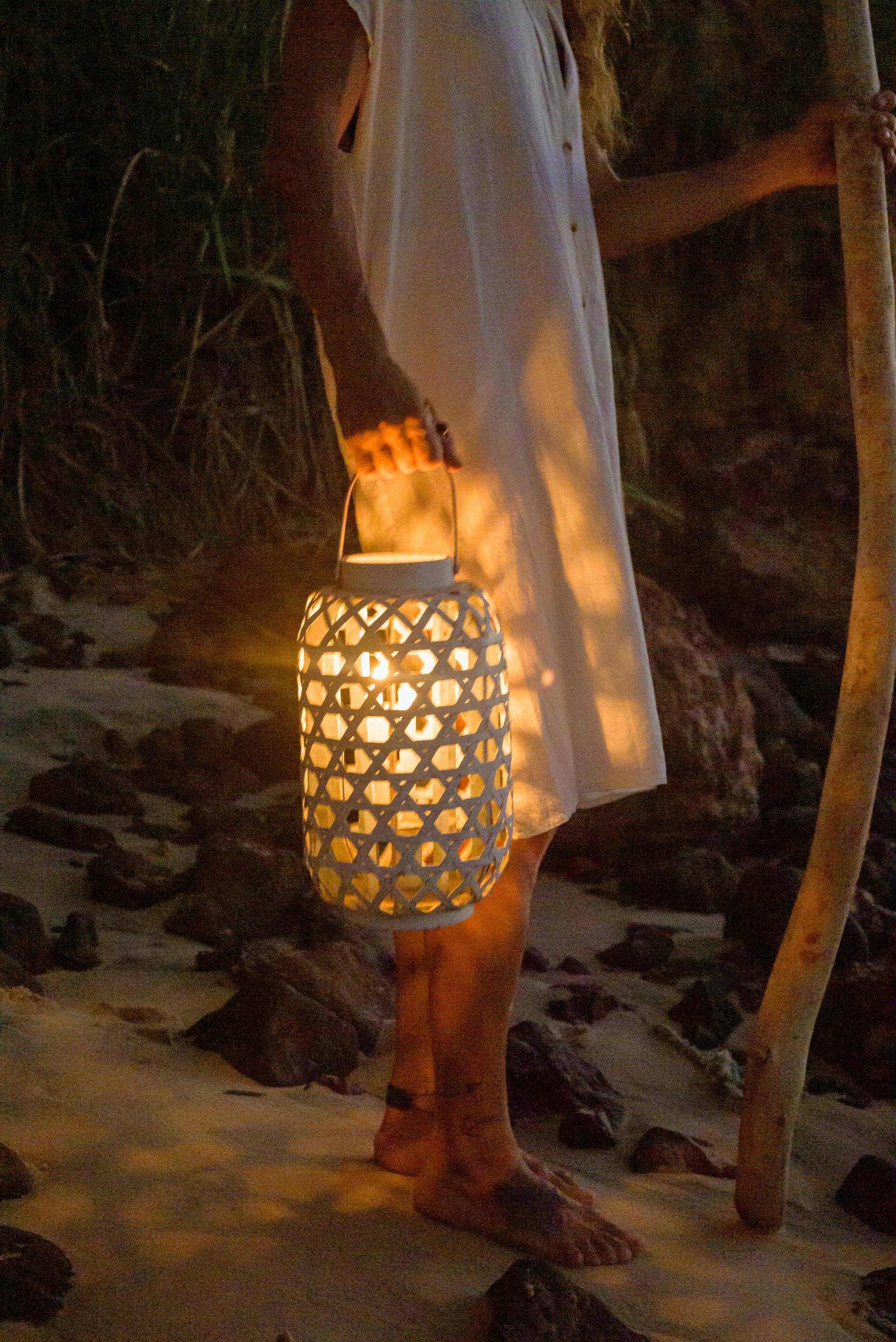 Una mujer de pie en la playa sujetando un farol | Fuente: Pexels