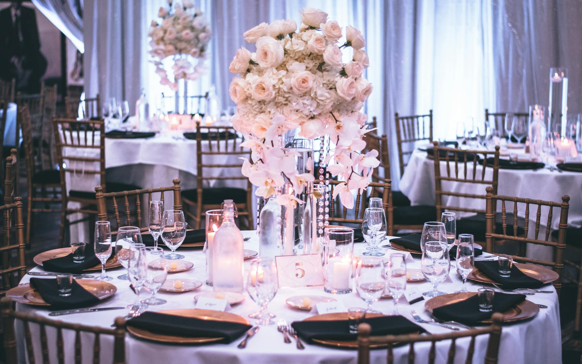 Una lujosa mesa de boda puesta con sillas doradas, platos negros y un centro floral | Fuente: Pexels