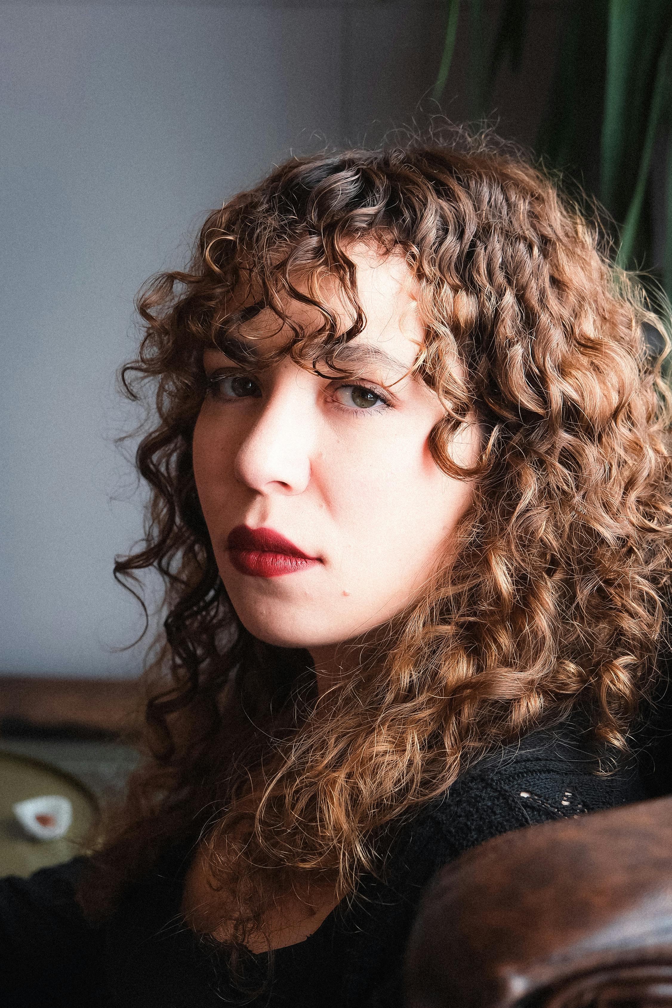 Una mujer pensativa con el pelo rizado y pintalabios rojo | Fuente: Pexels