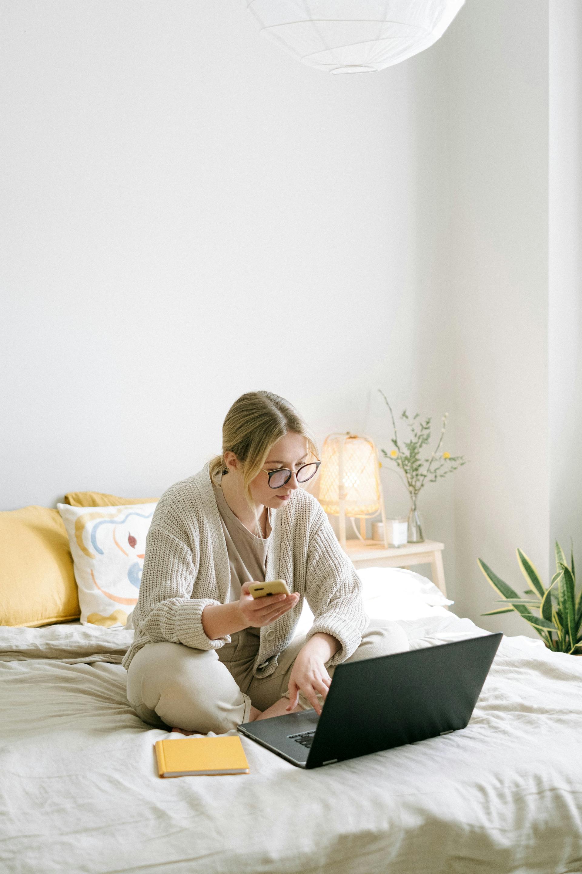 Una mujer utilizando un ordenador portátil y sujetando un teléfono | Fuente: Pexels