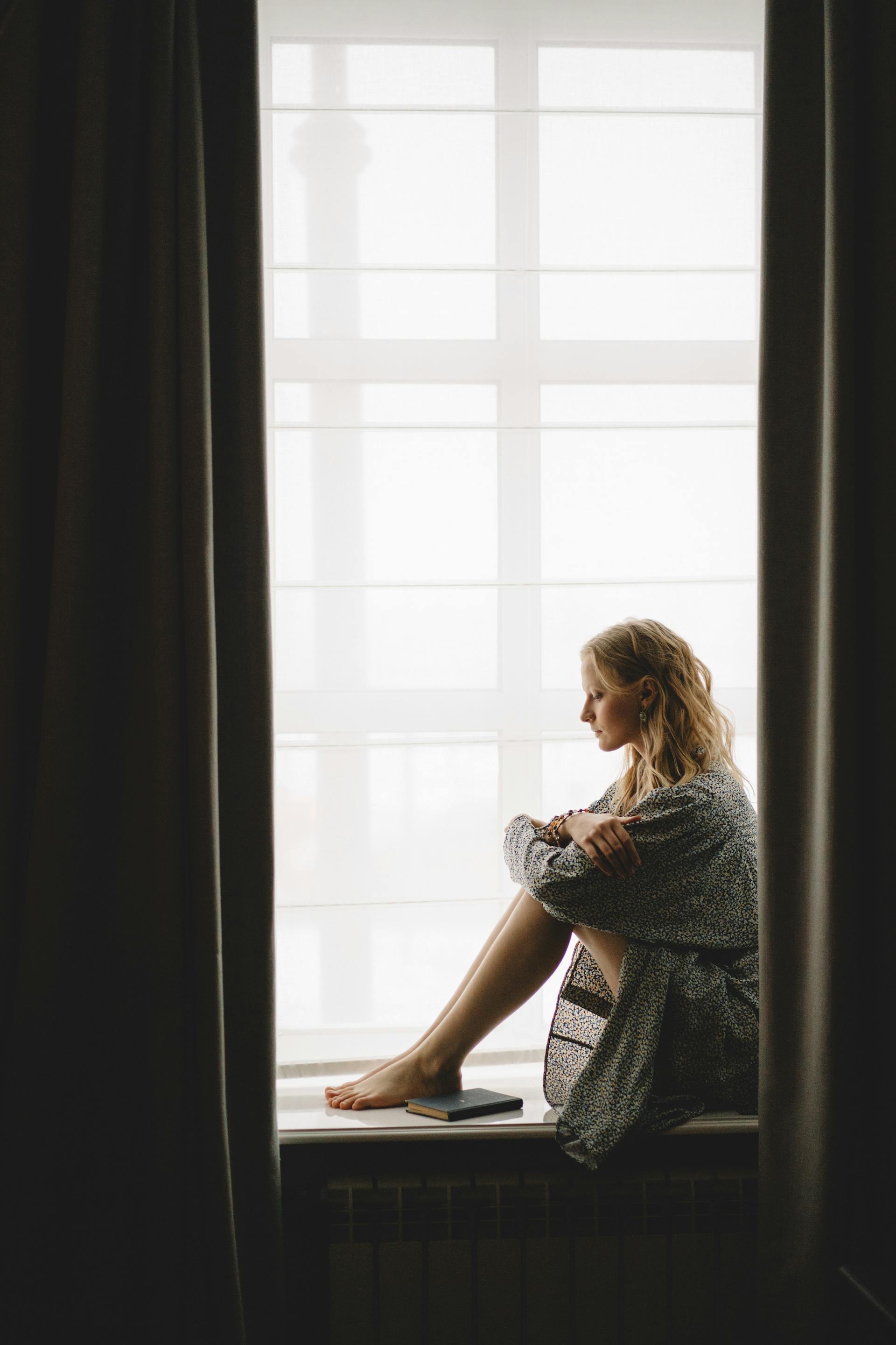 Una mujer pensativa sentada en el alféizar de la ventana | Fuente: Pexels