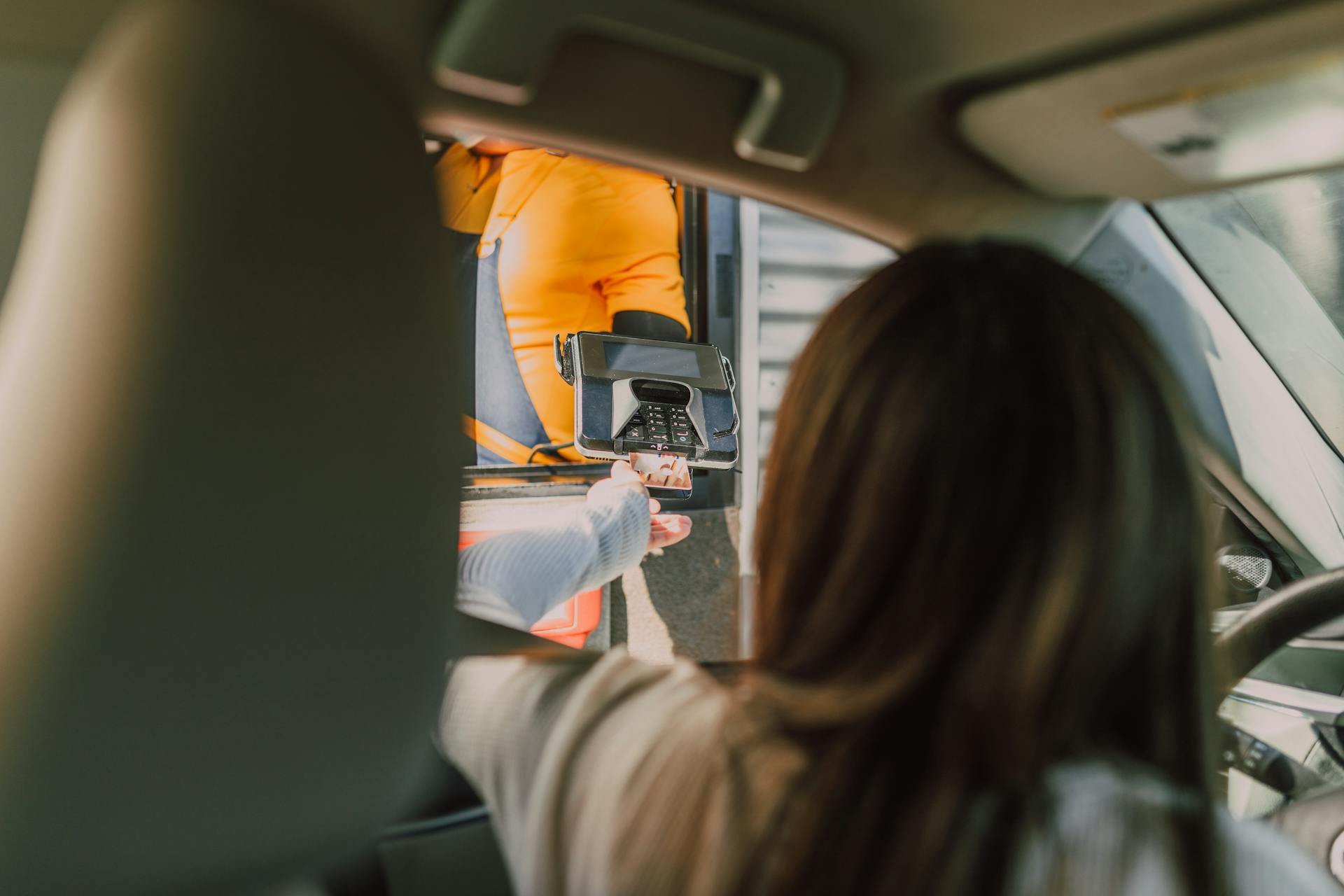 Una mujer sentada en su automóvil y realizando un pago en un servicio desde el auto. | Fuente: Pexels