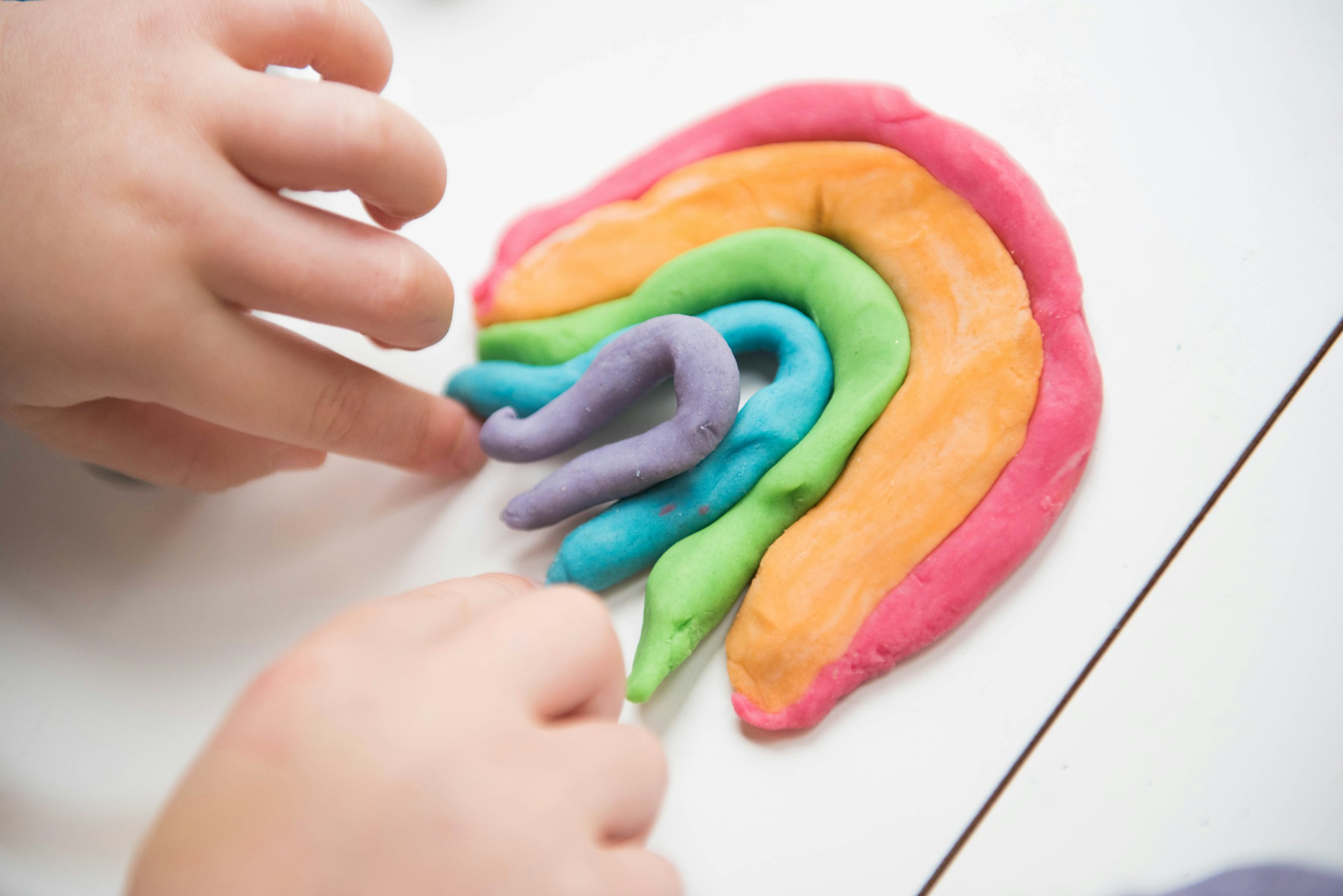 Primer plano de un niño jugando con tiras de colores de plastilina | Fuente: Unsplash
