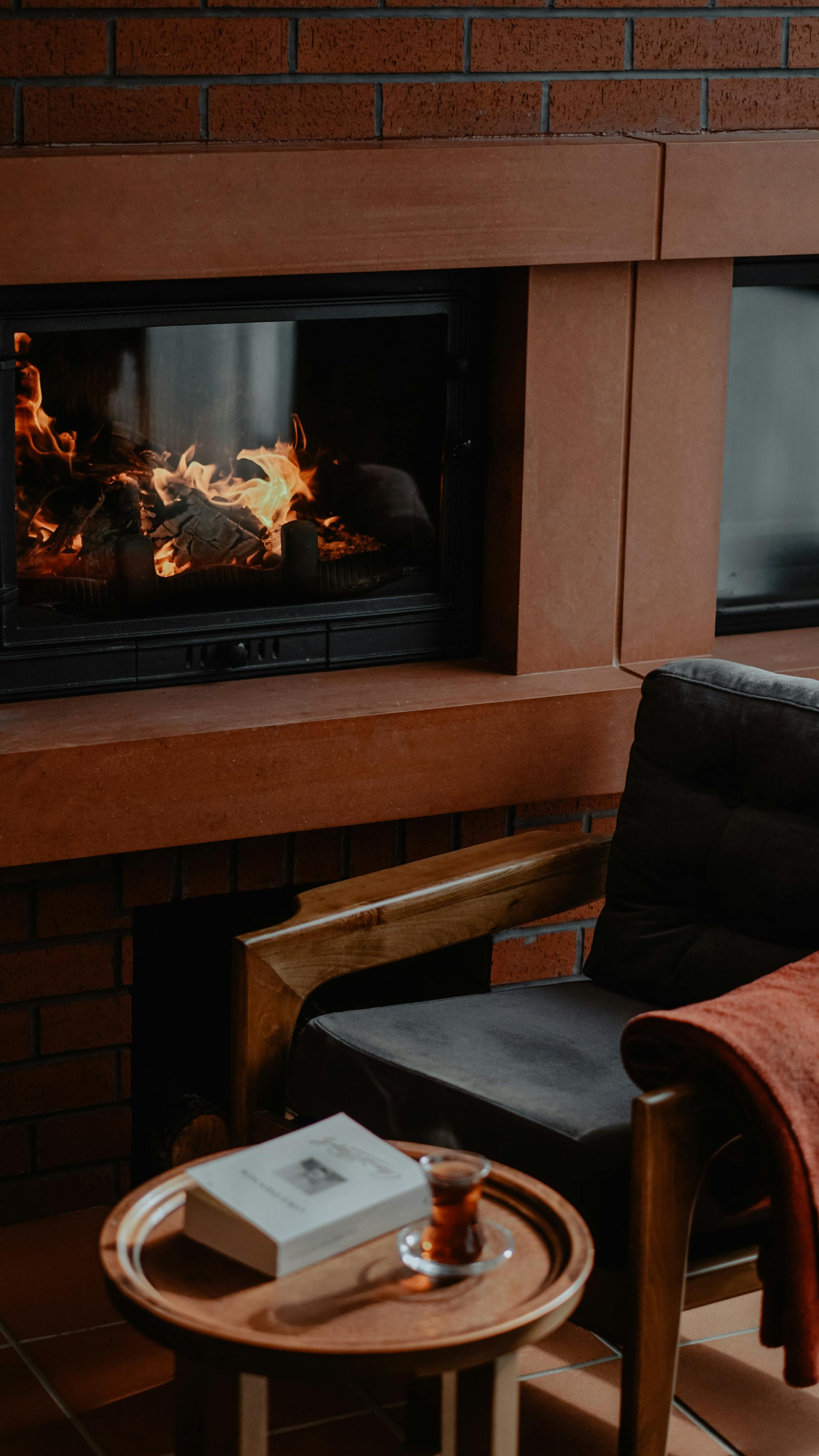 Un sillón y una mesa junto a una chimenea eléctrica | Fuente: Pexels