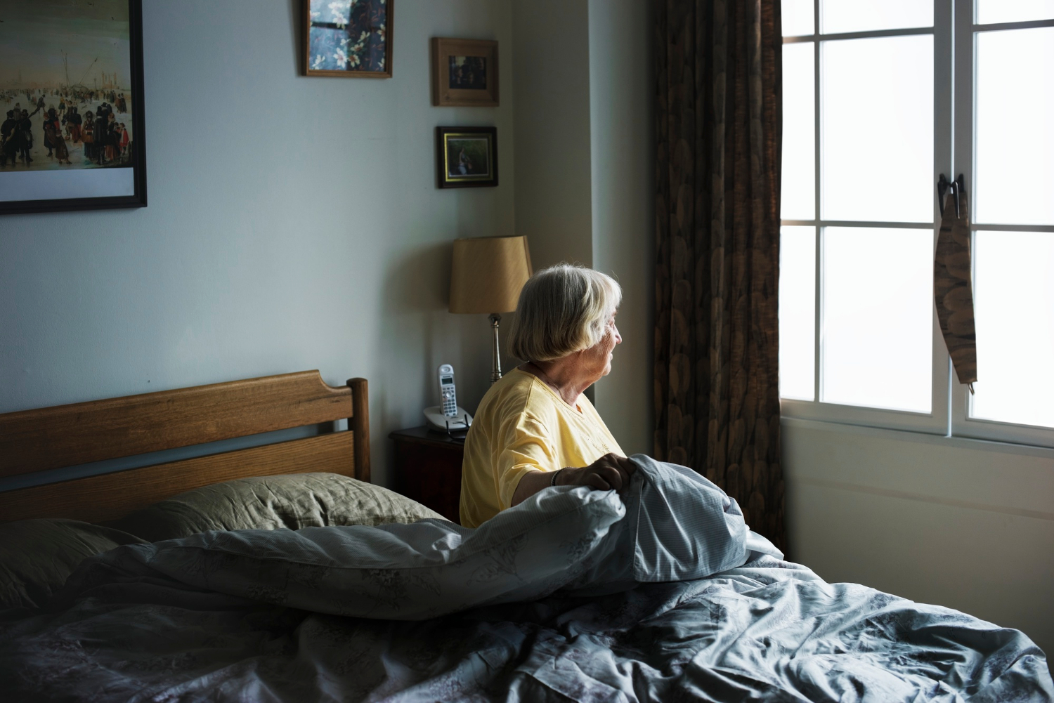 Una anciana solitaria sentada en su cama y mirando por la ventana | Fuente: Freepik