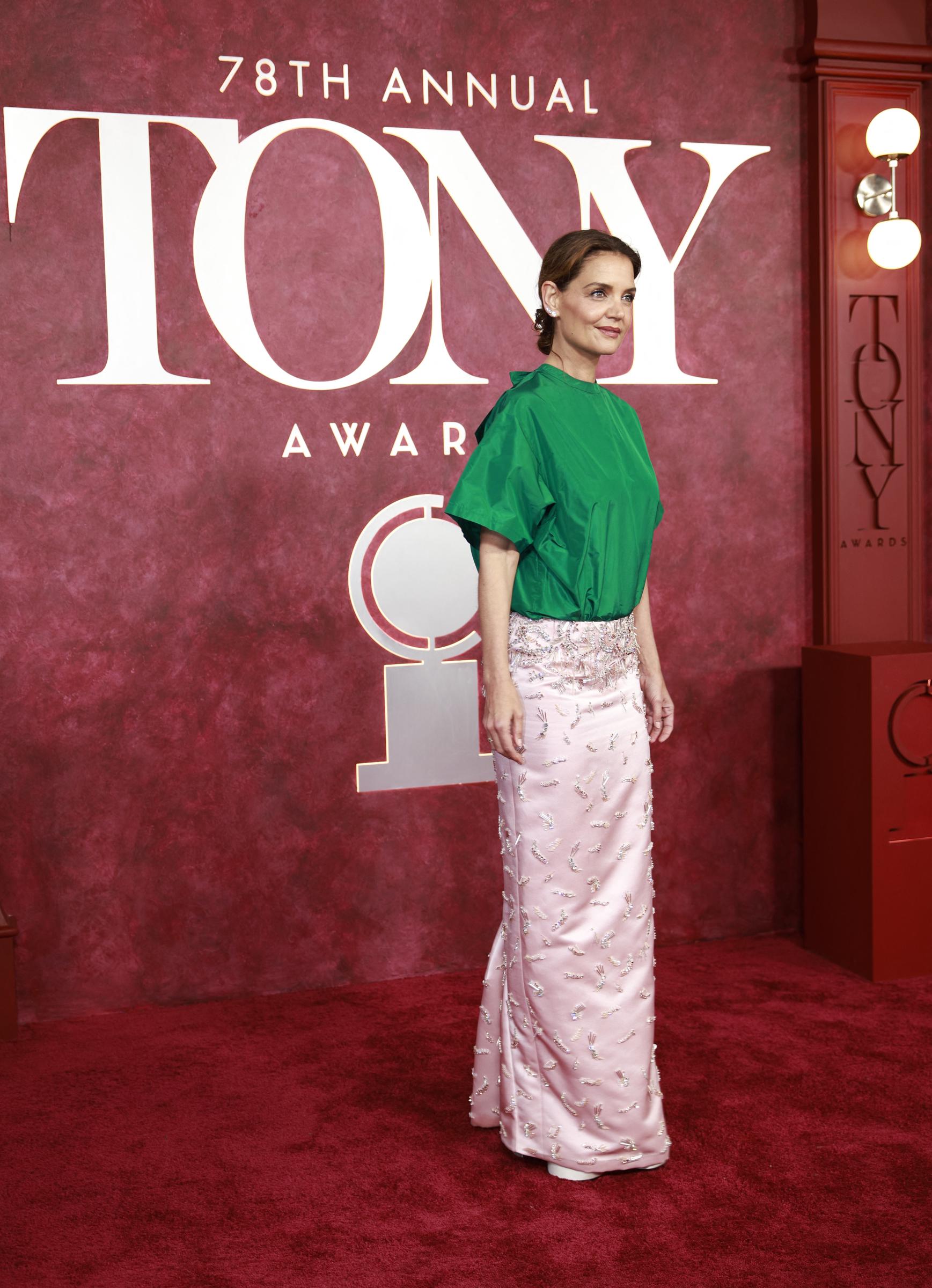 Con un pie ligeramente adelantado y una postura serena, Katie Holmes domina la alfombra roja con su conjunto verde y rosa. La foto capta tanto la elegancia como la audacia, reflejando las reacciones que su look suscitó en las redes sociales.