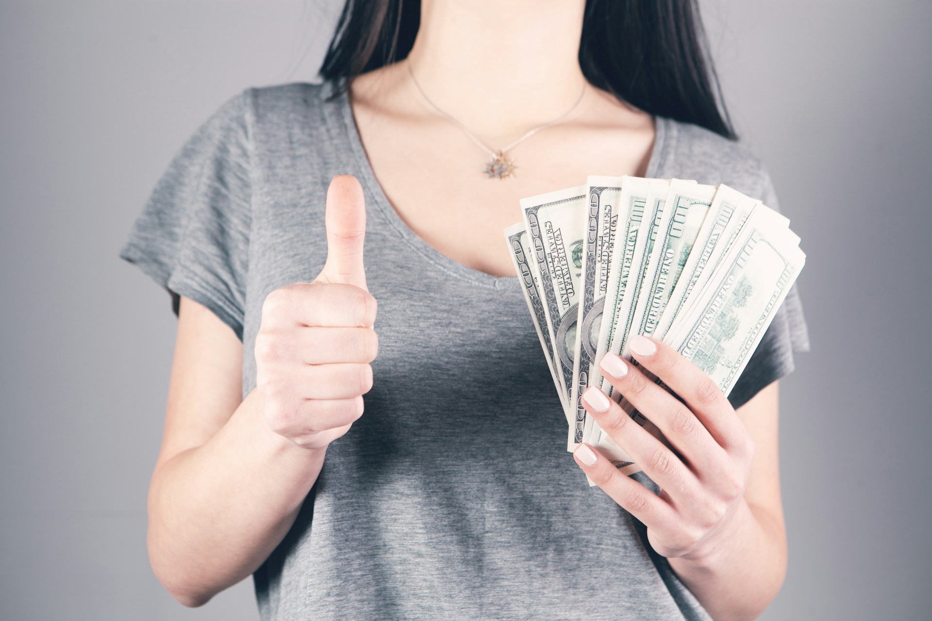 Una mujer sosteniendo dinero y dando un pulgar hacia arriba | Fuente: Unsplash