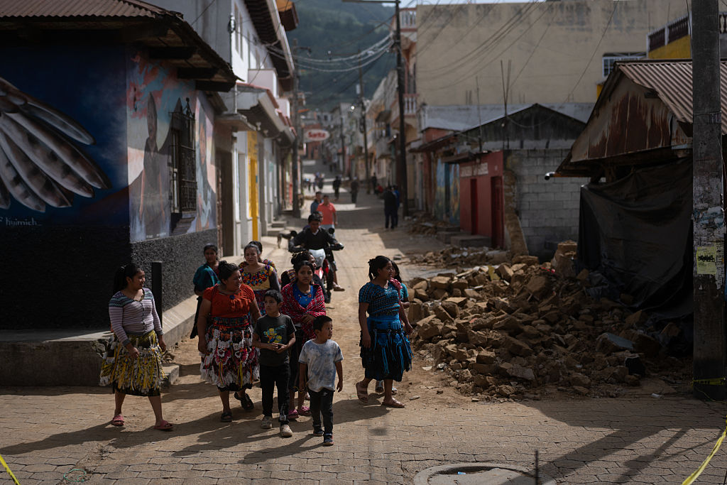 Personas caminan frente a una casa destruida durante una serie de sismos en Santa María de Jesús, Guatemala, el 9 de julio de 2025. | Foto: Getty Images