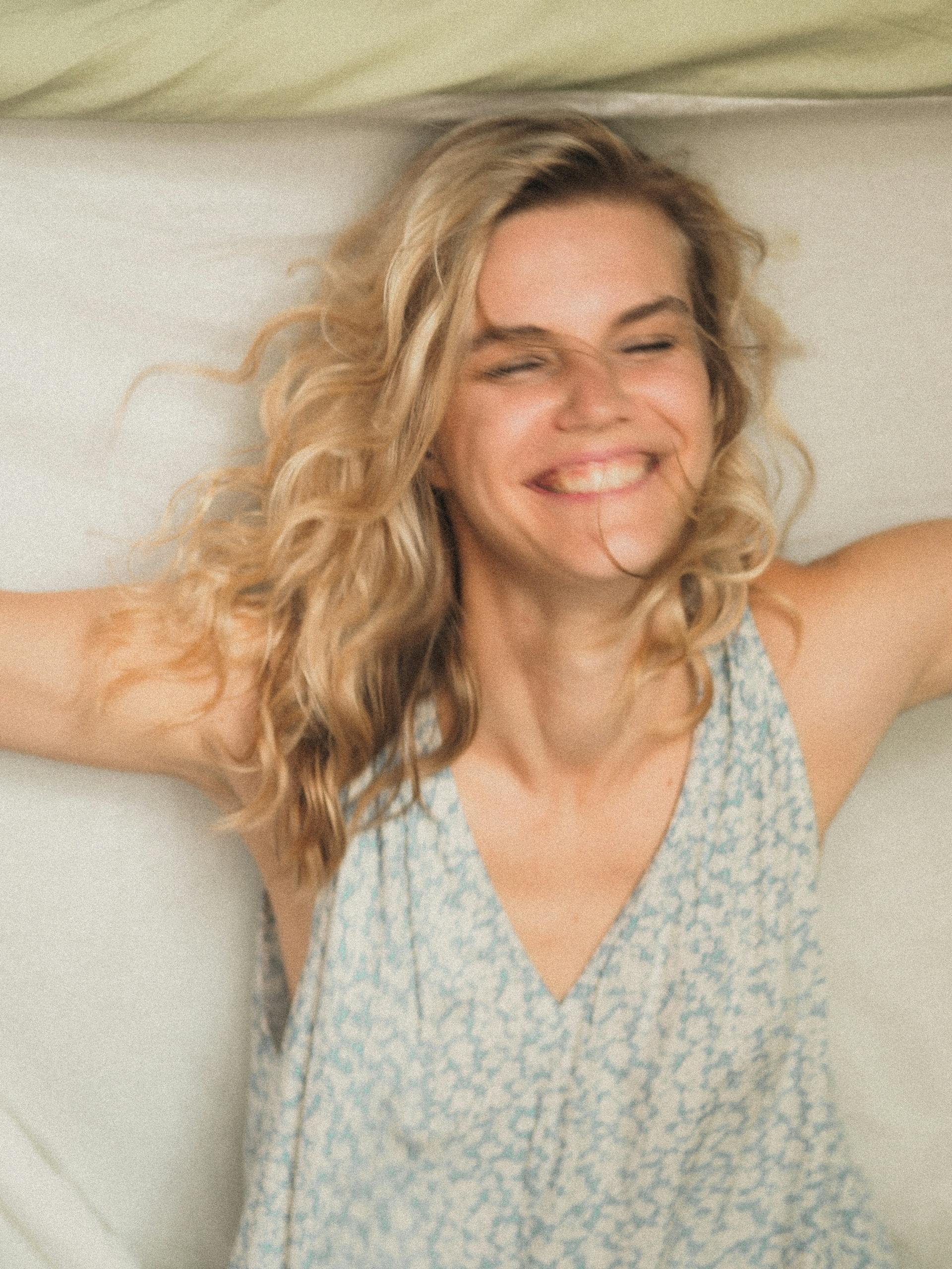 Una mujer tumbada en una cama riéndose | Fuente: Pexels
