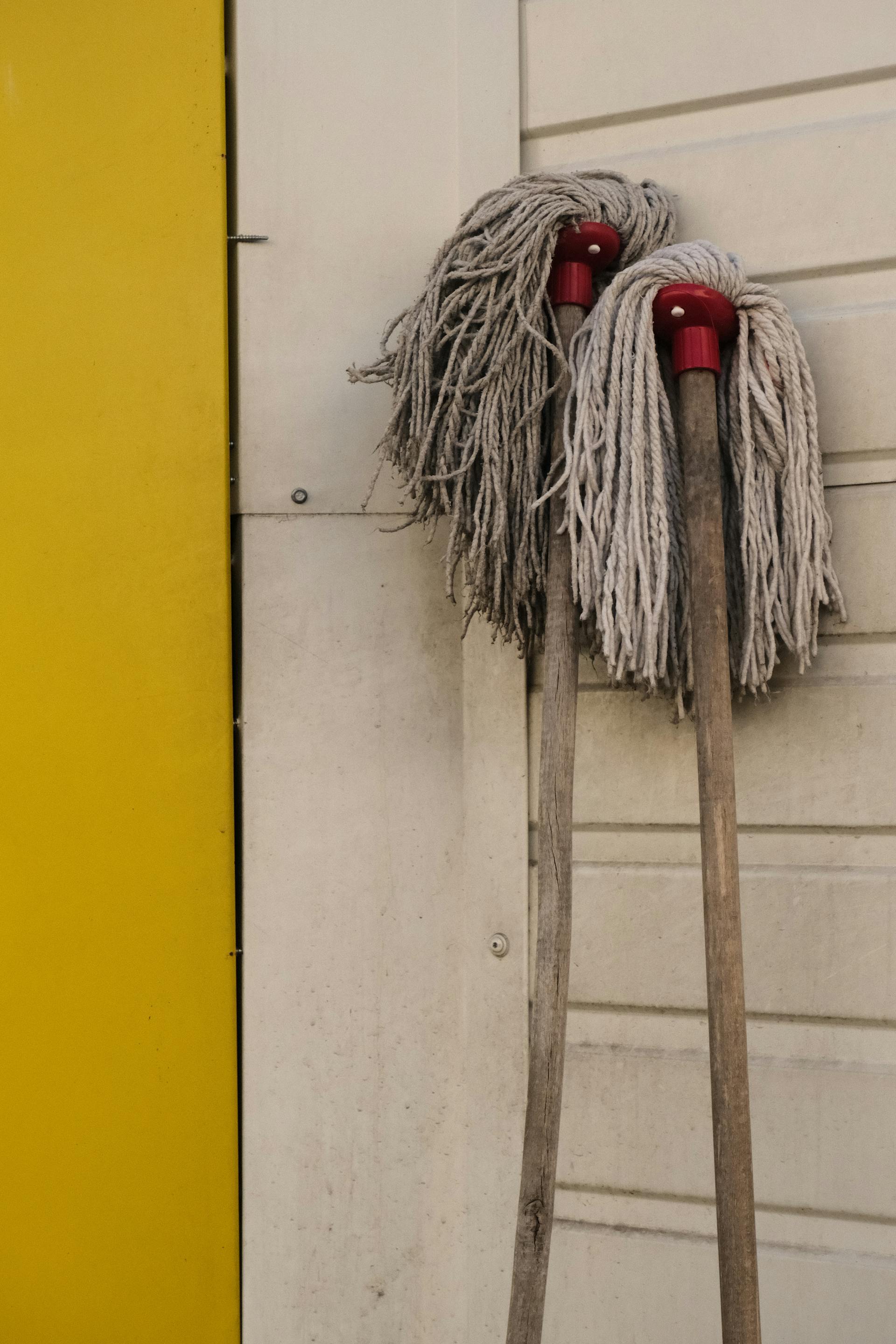 Dos fregonas desgastadas apoyadas en una pared | Fuente: Pexels