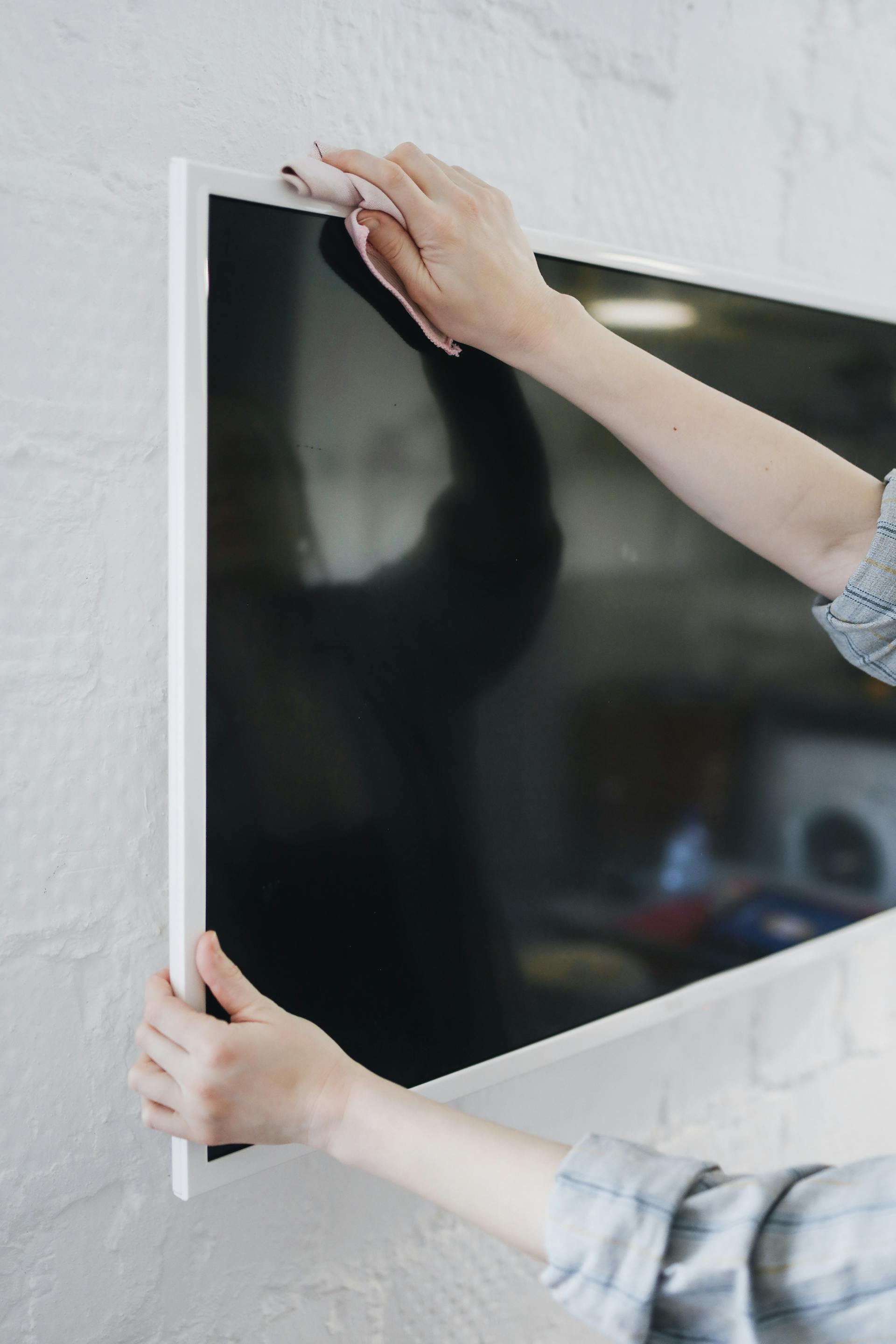 Primer plano de una persona limpiando un televisor montado en una pared | Fuente: Pexels