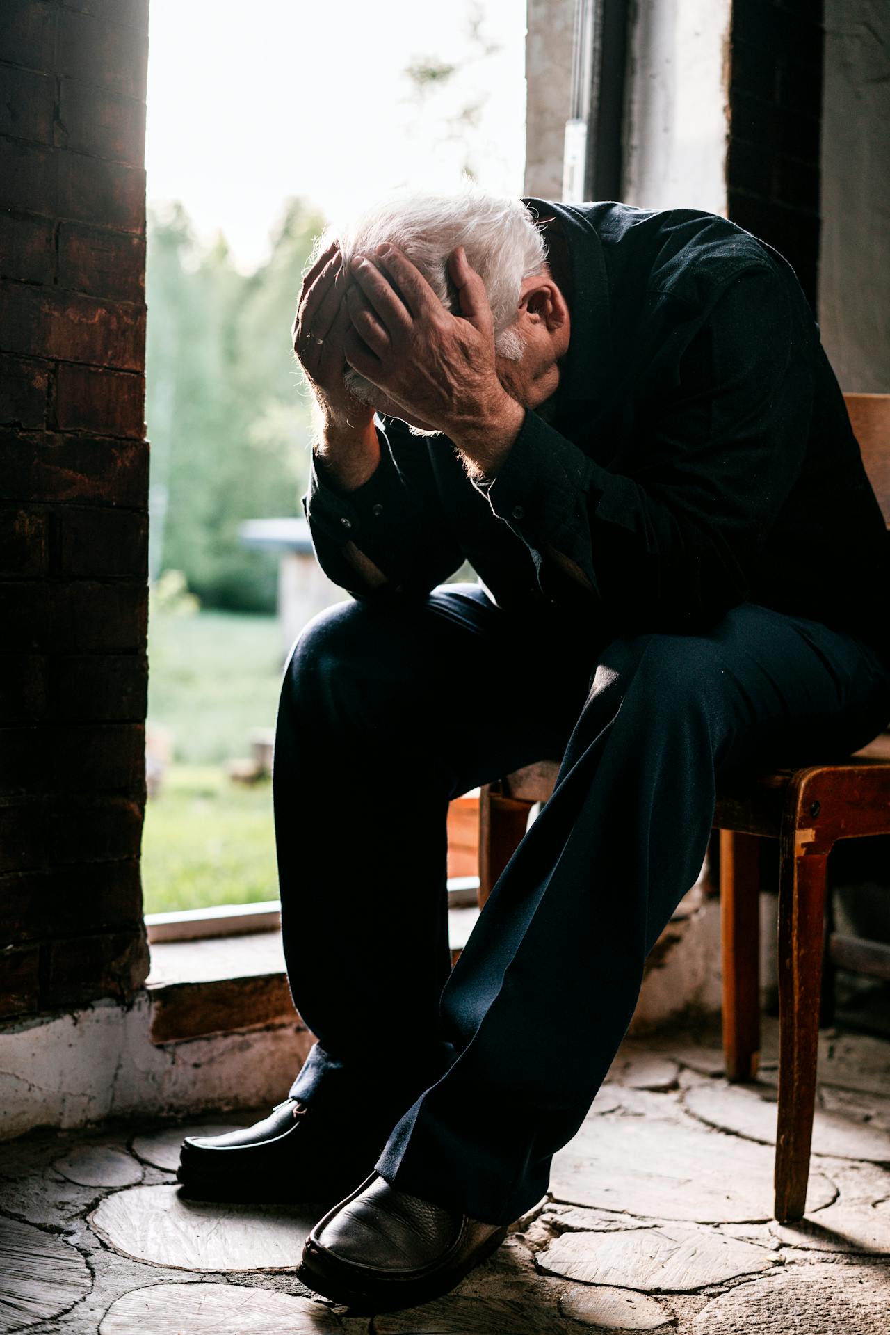 Un anciano triste sentado en una silla de madera marrón | Fuente: Pexels