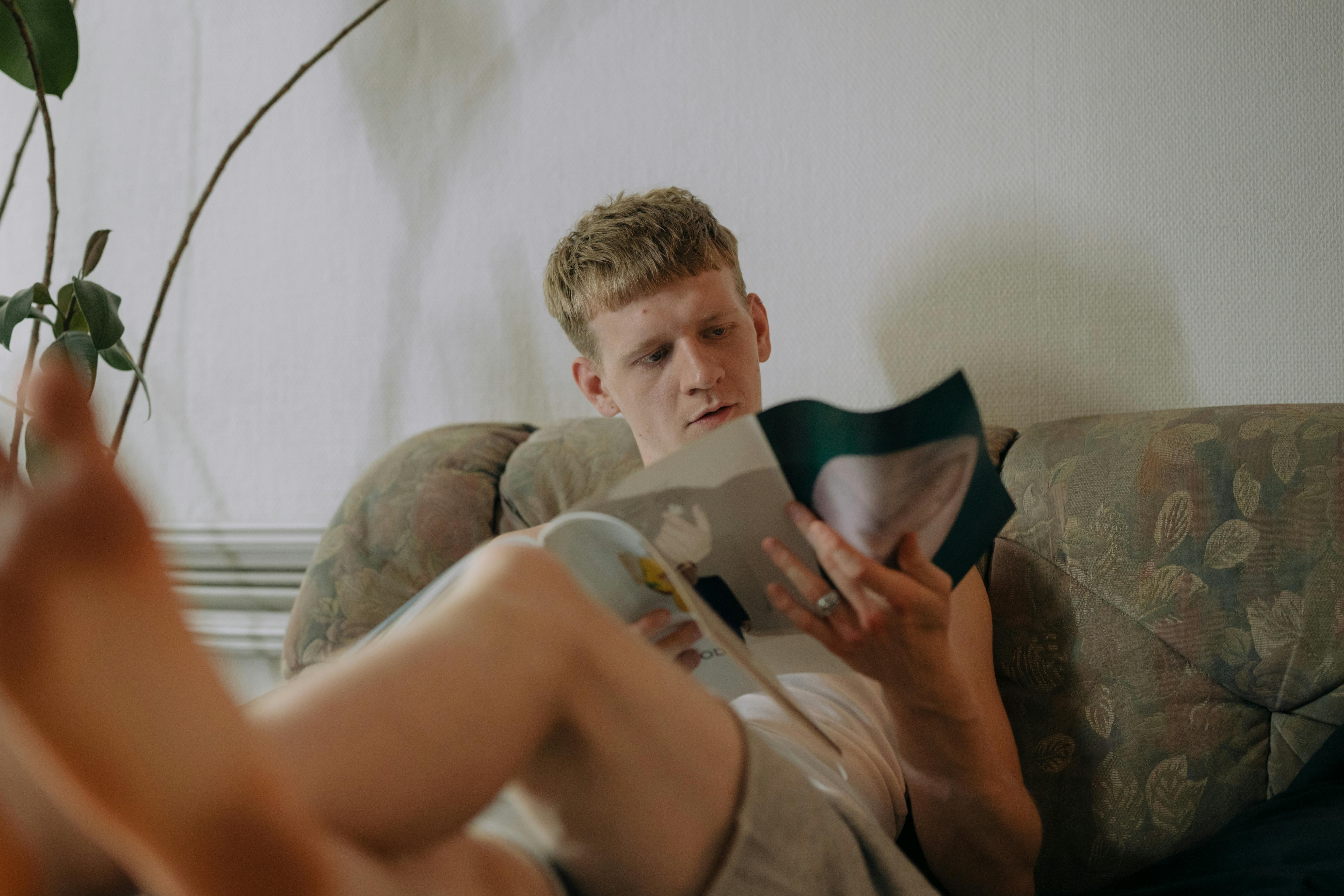 Hombre sentado en el sofá leyendo una revista | Fuente: Pexels