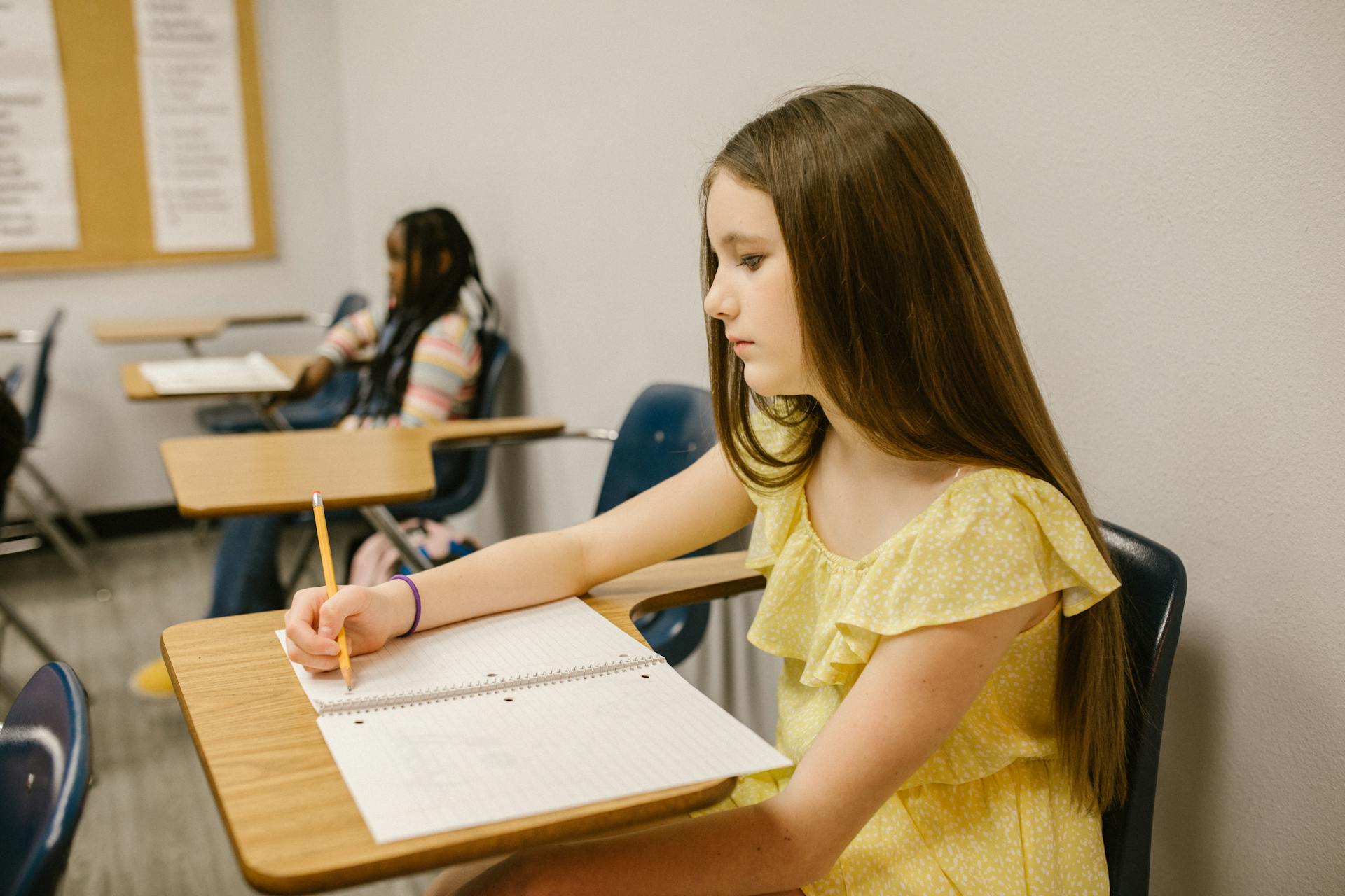 Una niña angustiada sentada en su clase y escribiendo en su cuaderno | Fuente: Pexels