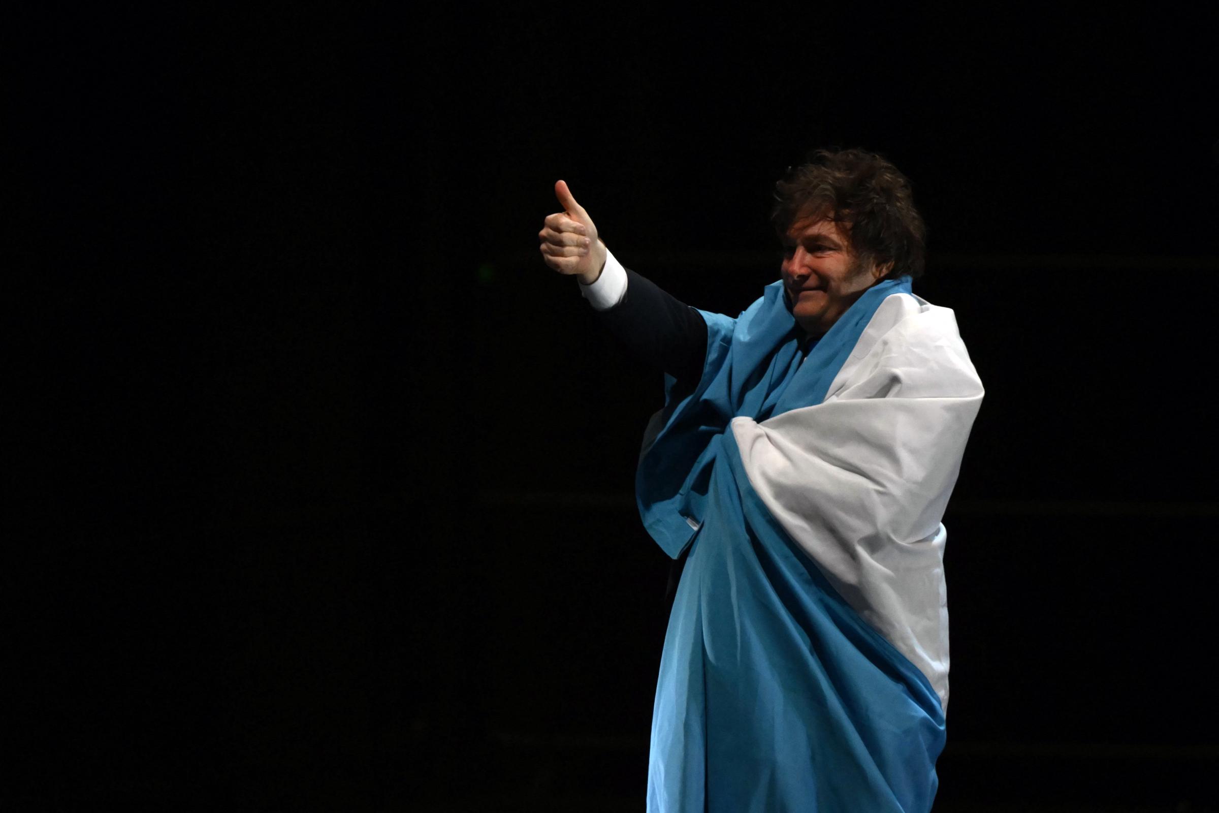 El presidente de Argentina, Javier Milei, levanta el pulgar envuelto en la bandera argentina durante la presentación de su nuevo libro, "La construcción del milagro", en el Movistar Arena de Buenos Aires el 6 de octubre de 2025. | Fuente: Getty Images