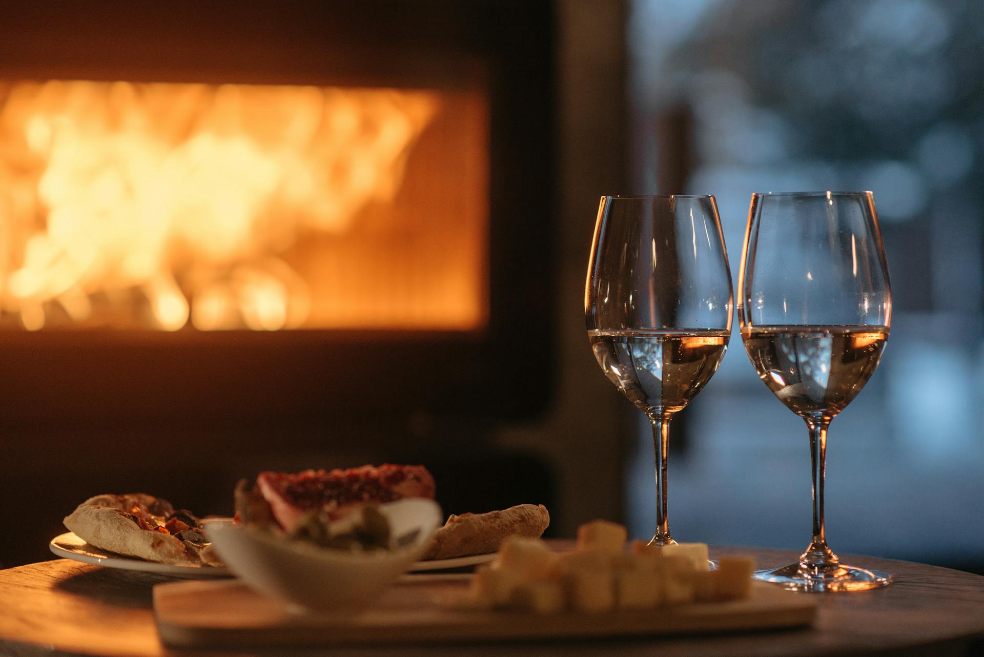 Dos copas de vino junto a un plato de comida frente a la chimenea | Fuente: Pexels