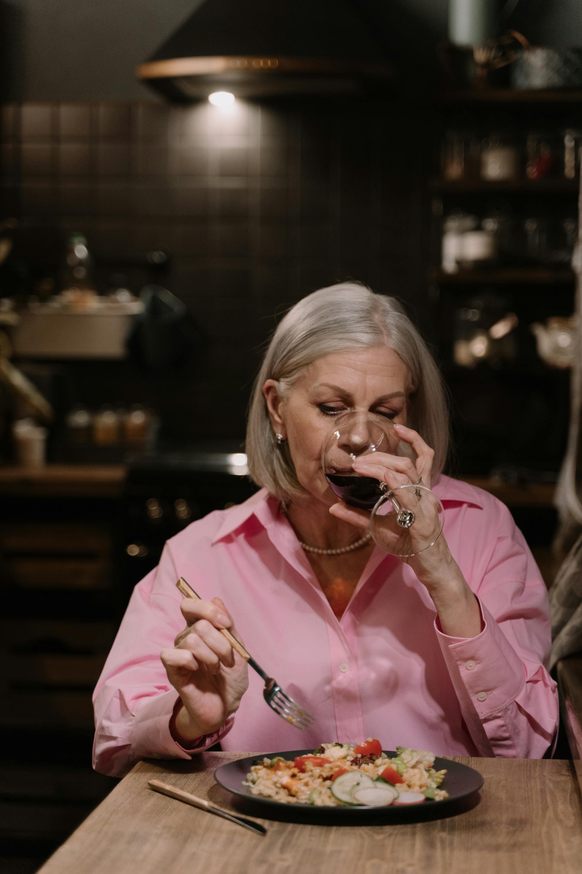 Una mujer mayor bebiendo vino mientras cena | Fuente: Pexels