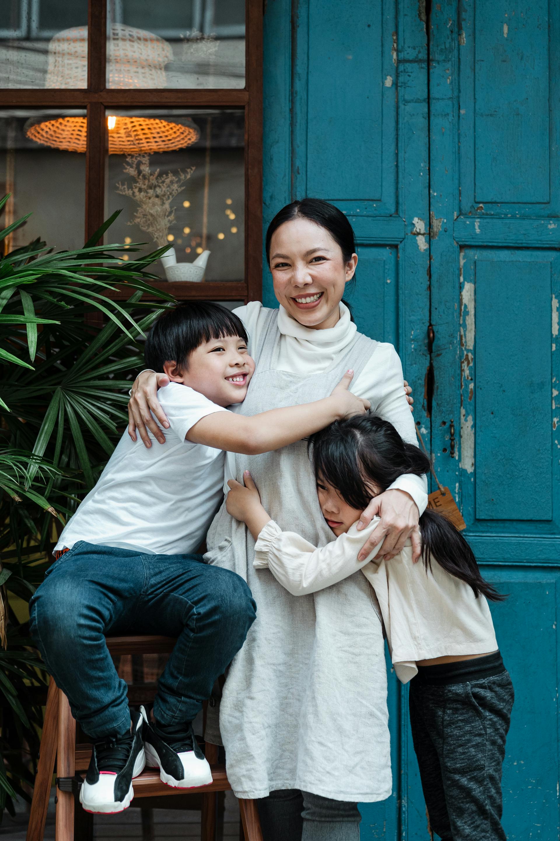 Una madre feliz abrazando a sus dos hijos delante de una puerta azul | Fuente: Pexels