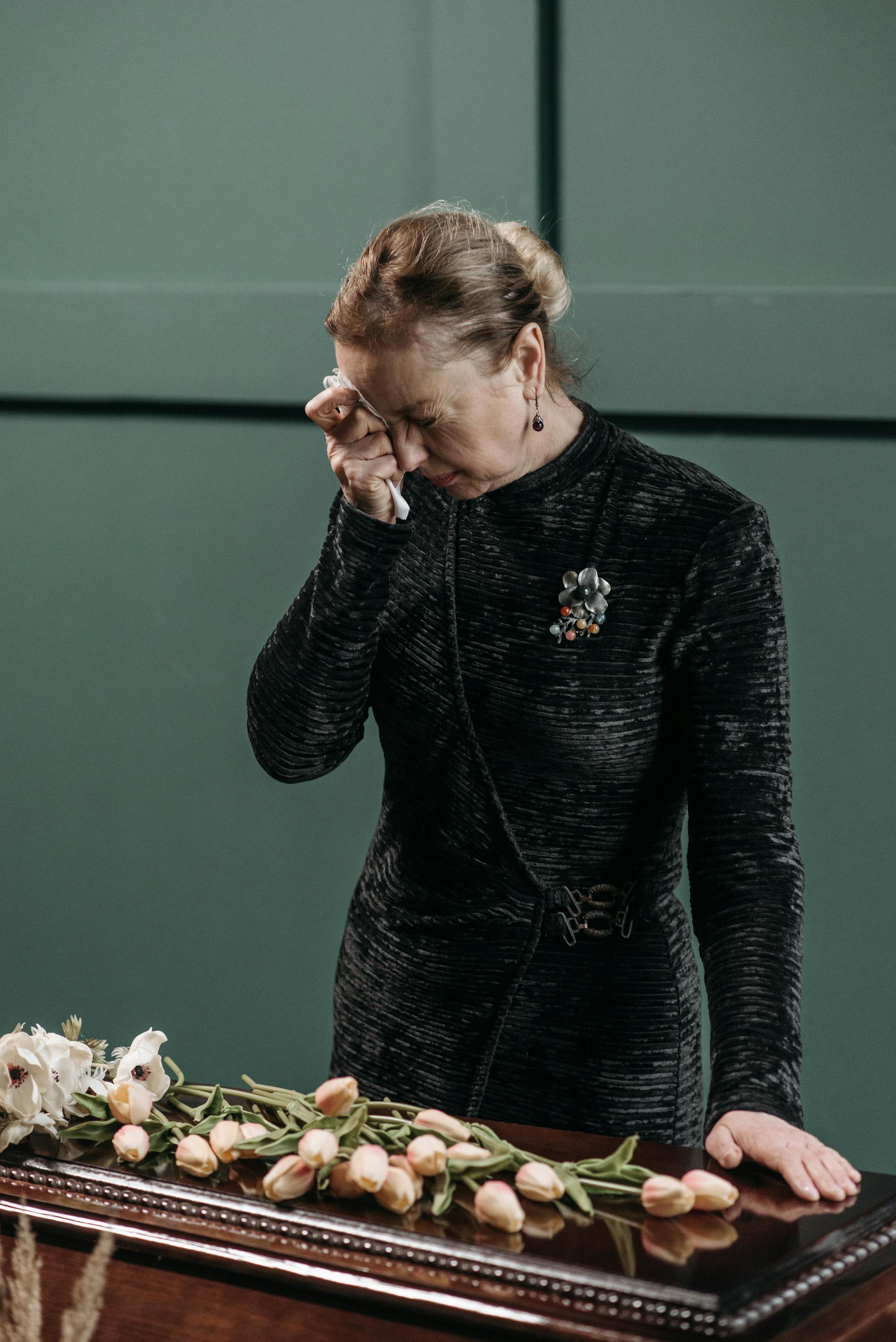 Una mujer madura llorando con un vestido negro junto a un ataúd | Fuente: Pexels