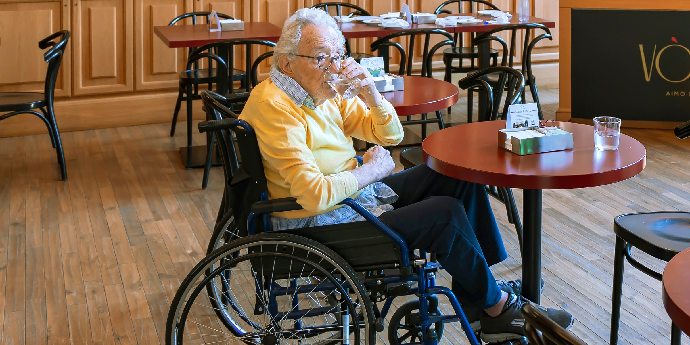 Un anciano en silla de ruedas bebiendo agua en un restaurante | Fuente: Shutterstock