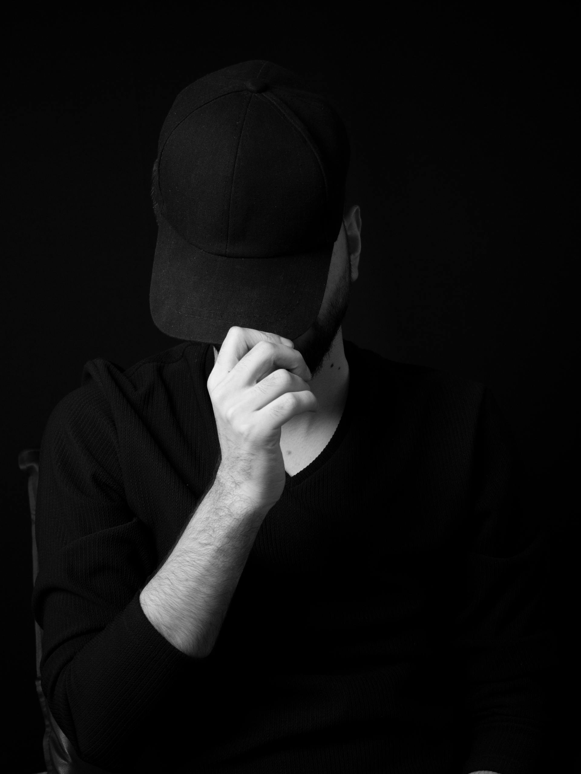 Foto en escala de grises de un hombre ocultando su rostro con su gorra | Fuente: Pexels
