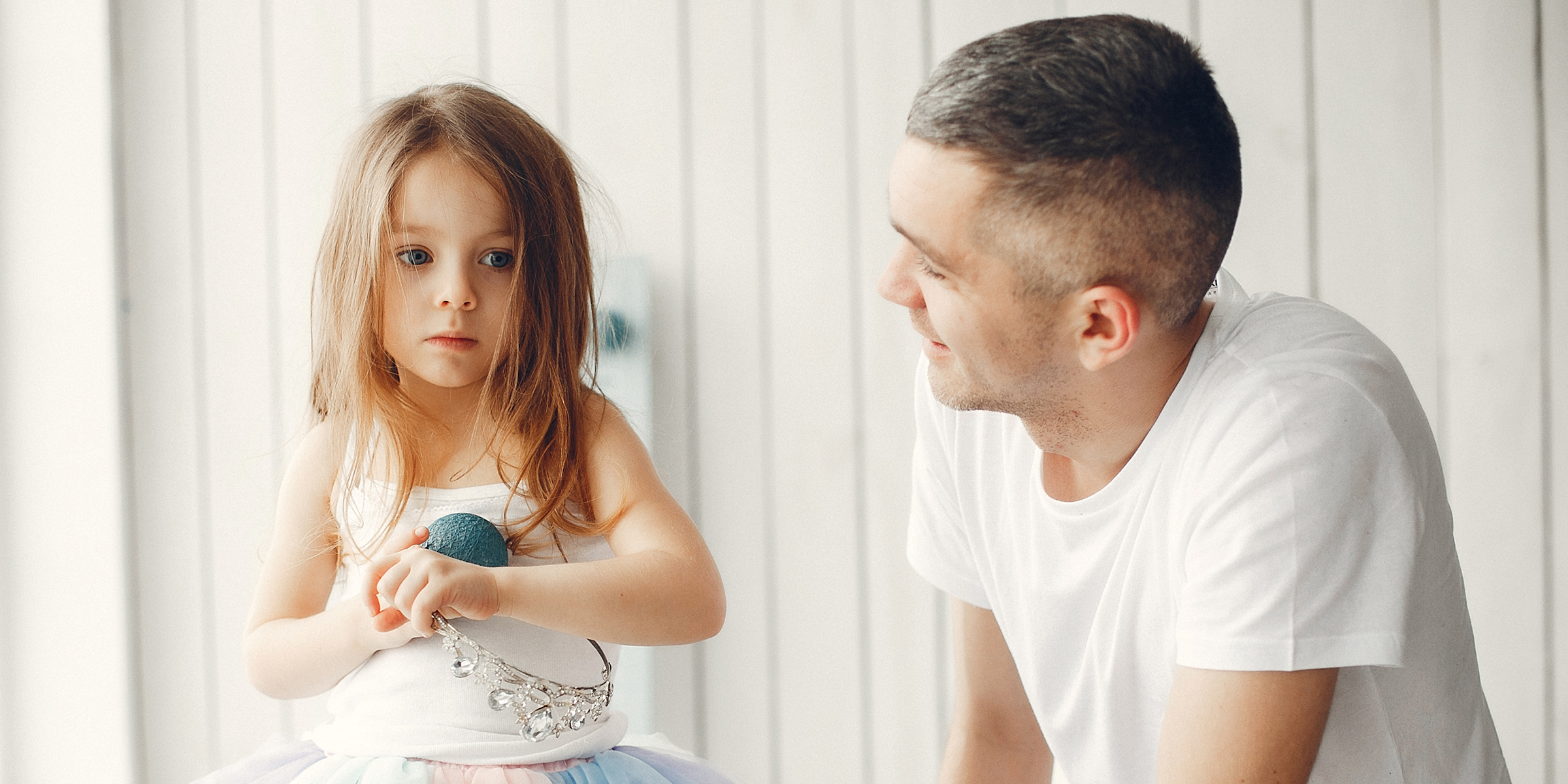 Un padre sonríe suavemente a su hija mientras ella mira fijamente al frente, perdida en sus pensamientos | Fuente: Shutterstock