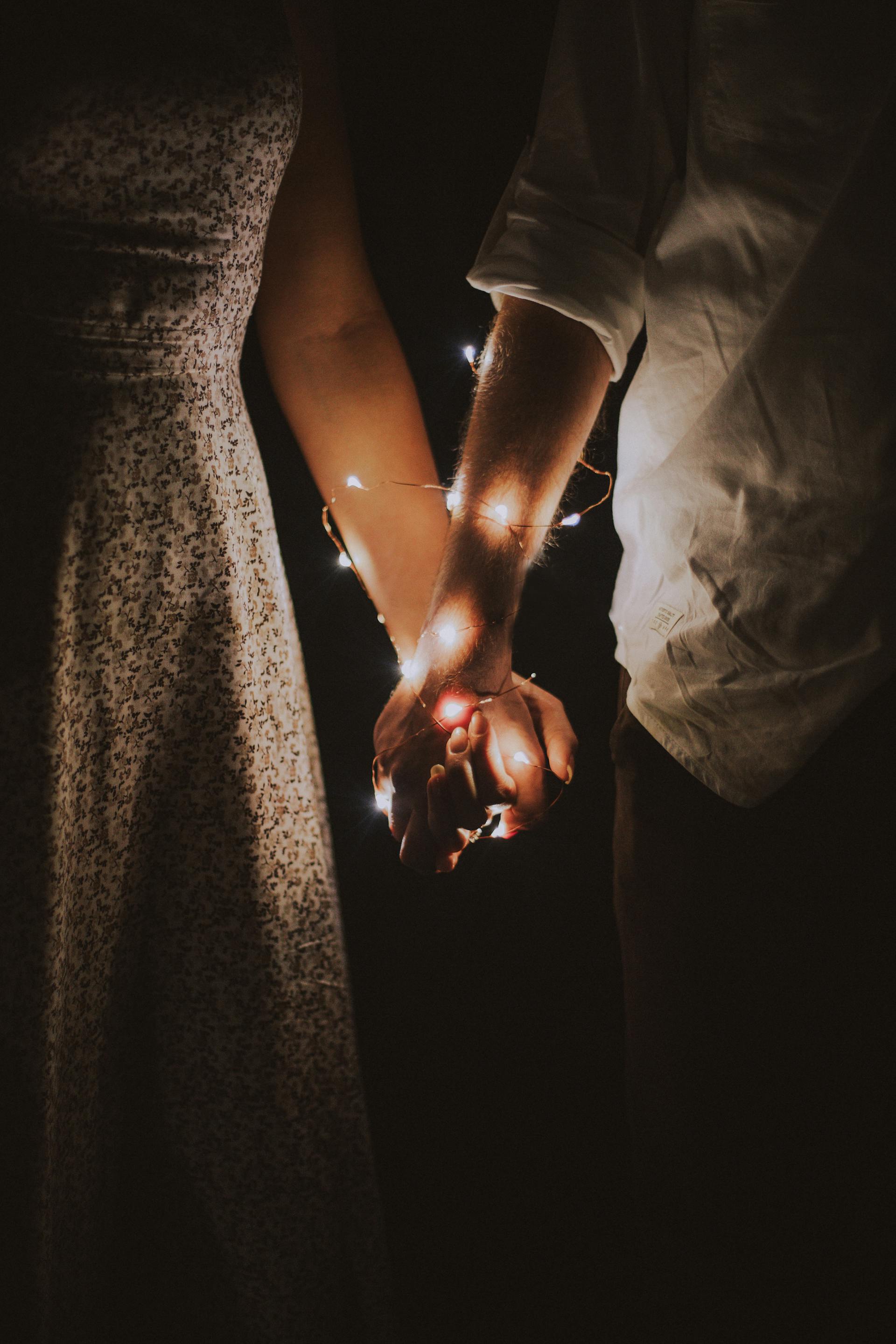 Una pareja tomada de la mano envuelta con cuerdas de luces | Fuente: Pexels