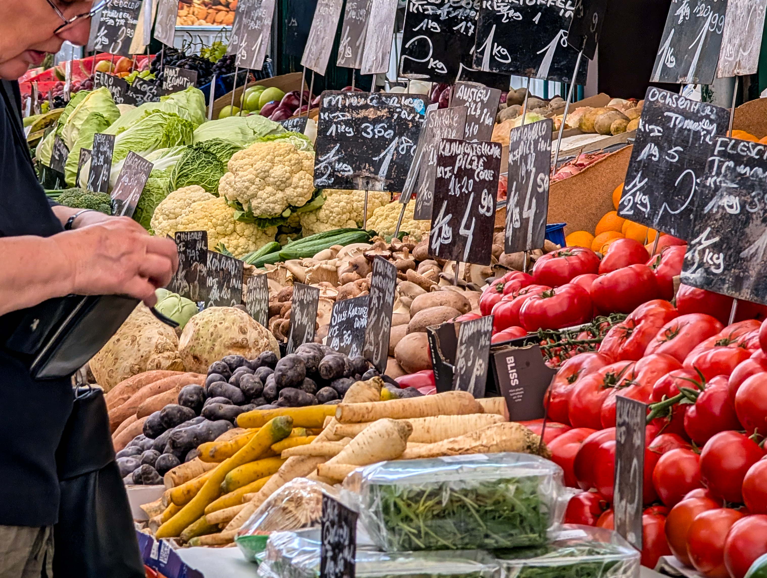 Verduras frescas y carteles de precios escritos a mano en un puesto del mercado | Fuente: Getty Images