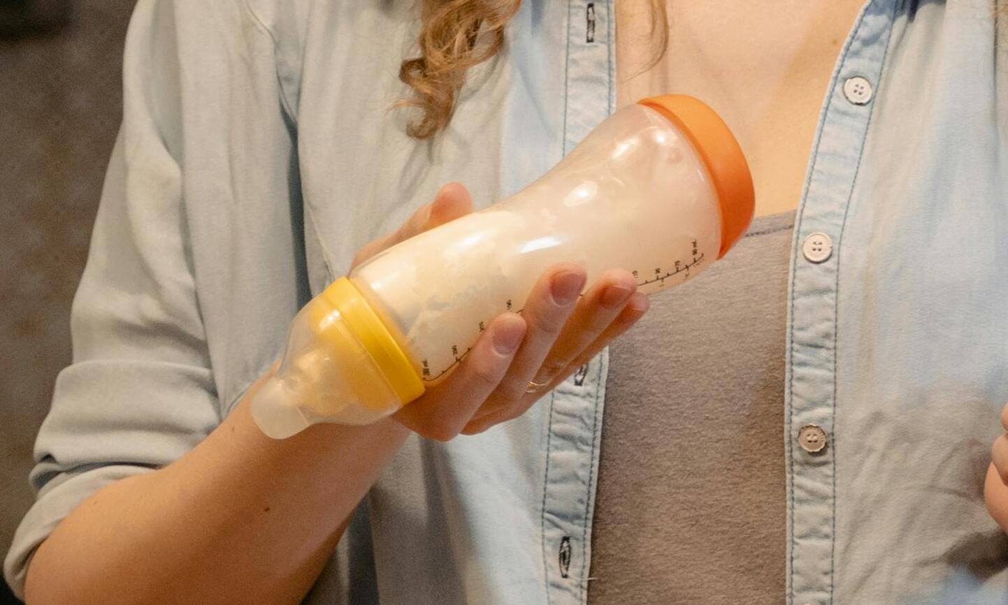 Una mujer con camisa de jean sostiene un biberón lleno de leche | Fuente: Pexels
