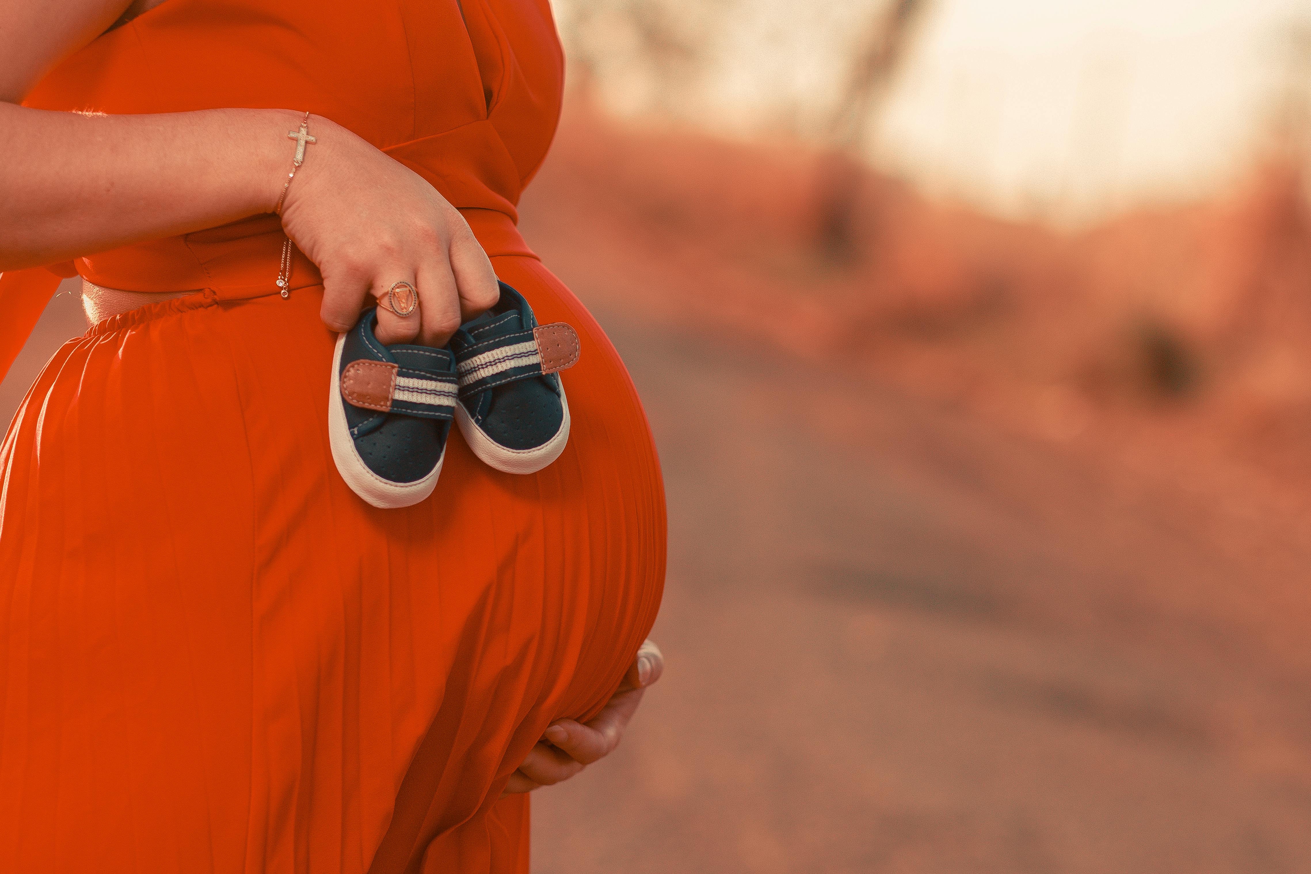 Una mujer embarazada con zapatos de bebé en la mano | Fuente: Pexels