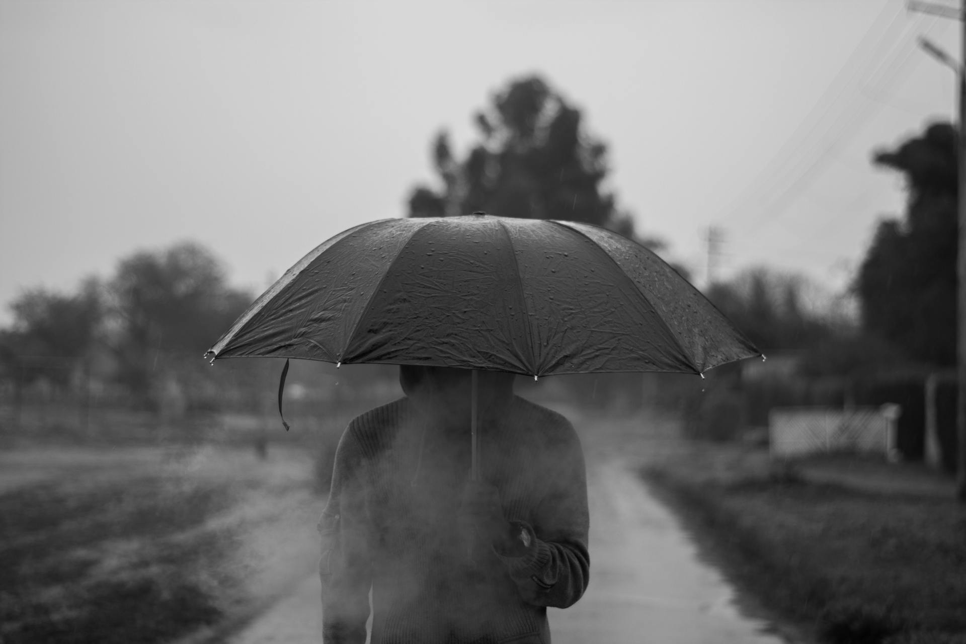 Foto en escala de grises de una persona con sudadera y paraguas en la mano | Fuente: Pexels