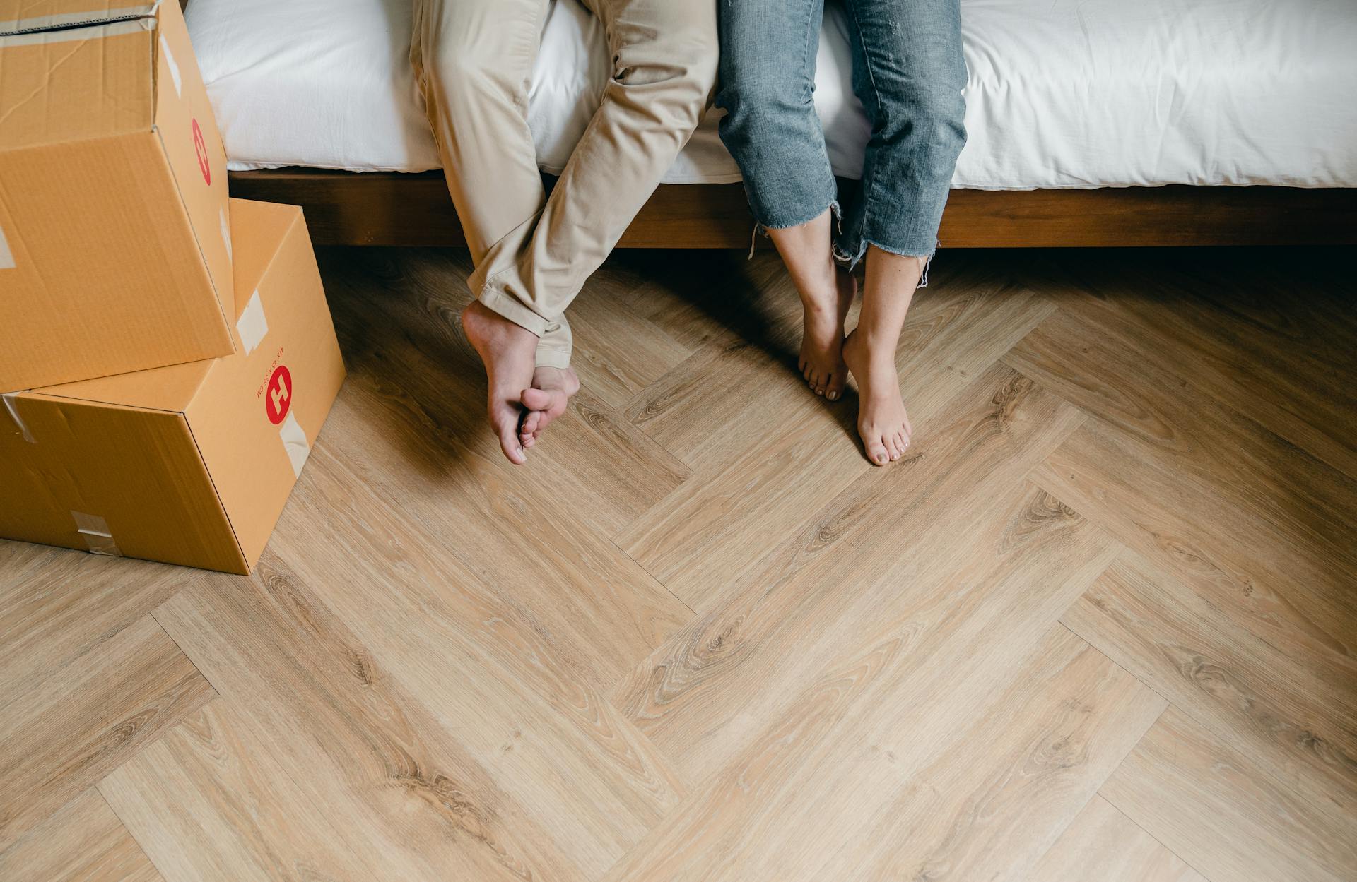 Primer plano de una pareja sentada en la cama con cajas de cartón a su alrededor | Fuente: Pexels
