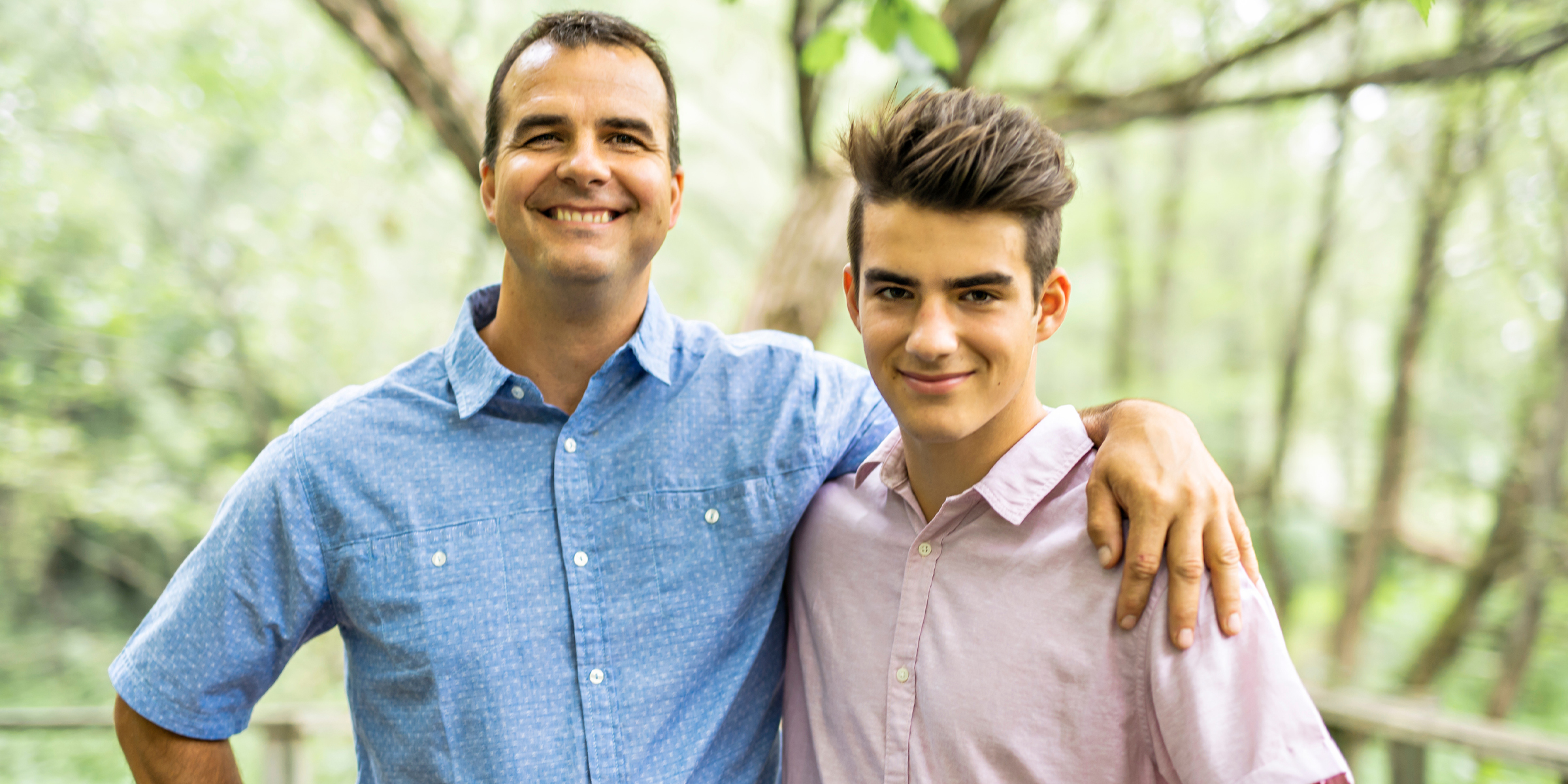 Un hombre sonriente y un adolescente posan juntos al aire libre en una zona boscosa | Foto: Shutterstock