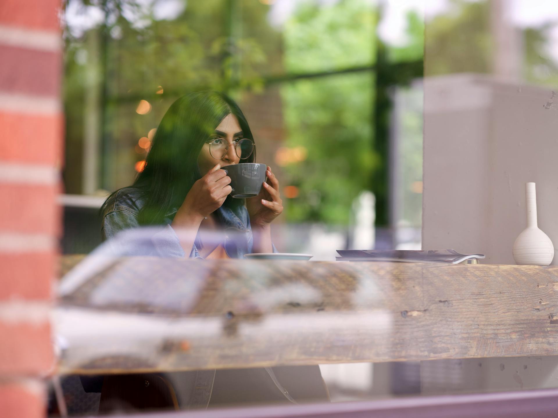 Una mujer sentada en una cafetería y bebiendo de una taza mientras mira al exterior desde la ventana | Fuente: Pexels