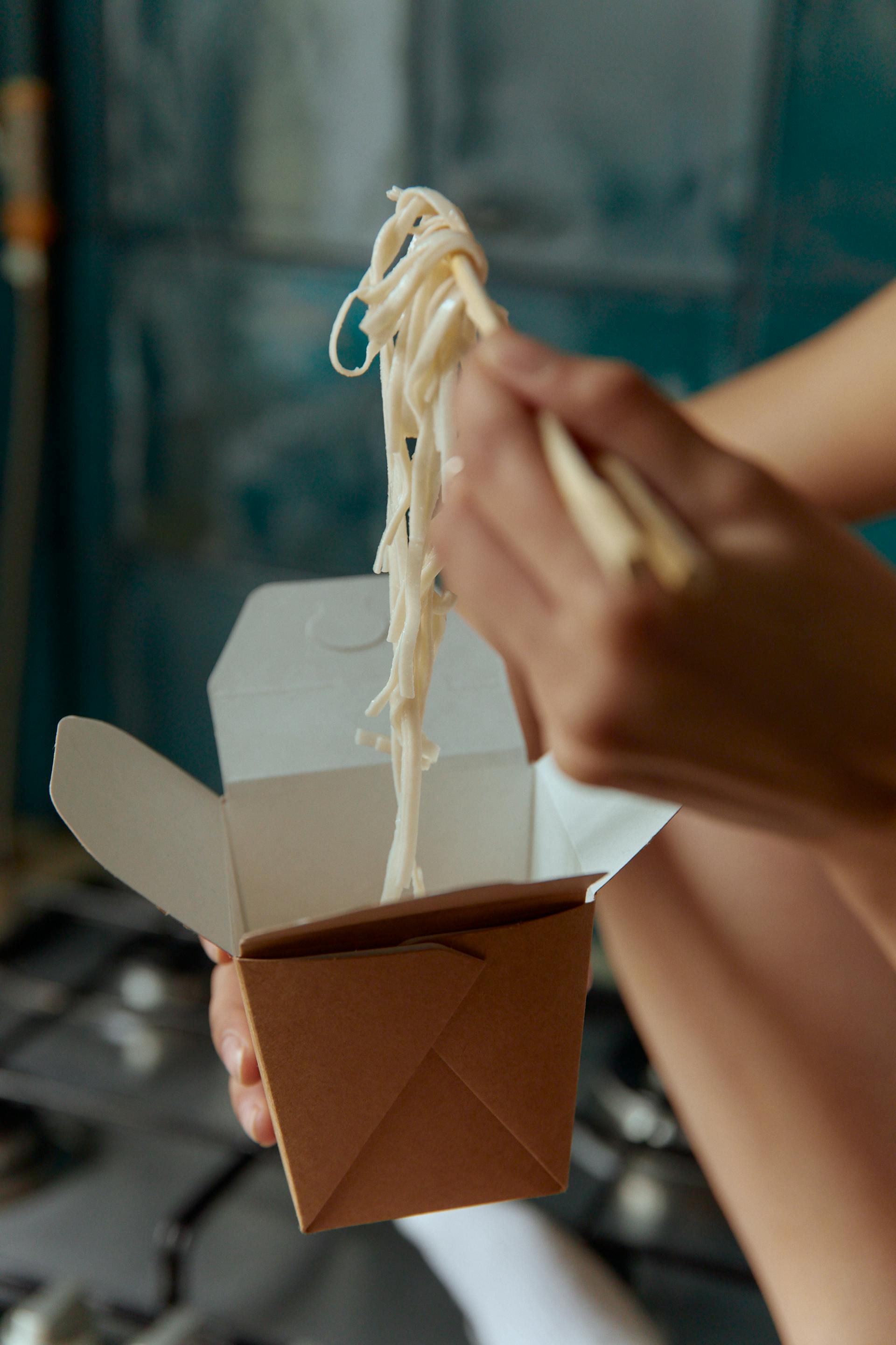 Una persona comiendo comida para llevar con palillos chinos | Fuente: Pexels