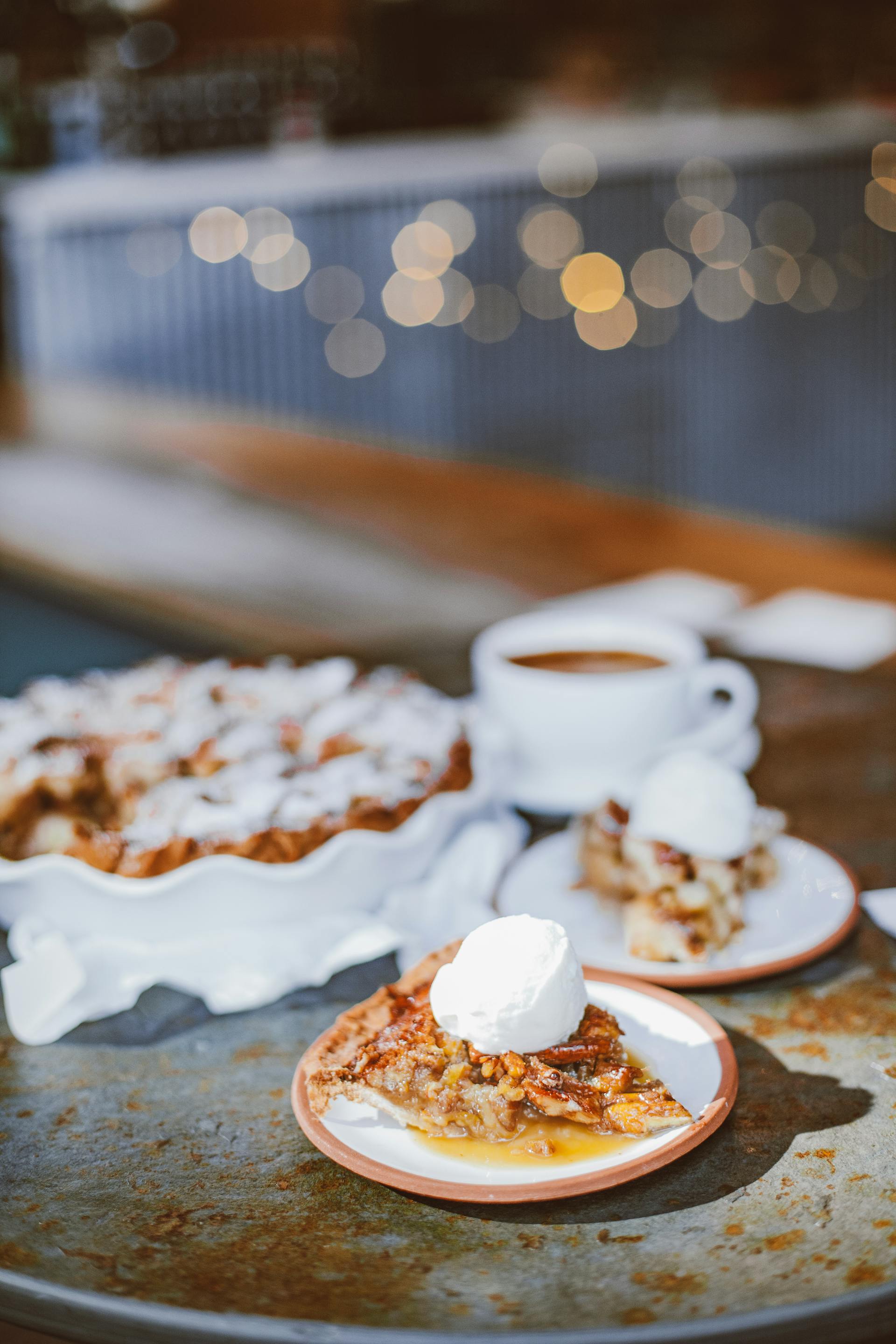 Una tarta de postre coronada con una bola de helado sobre una mesa con una taza de café y luces de cuerda de fondo | Fuente: Pexels