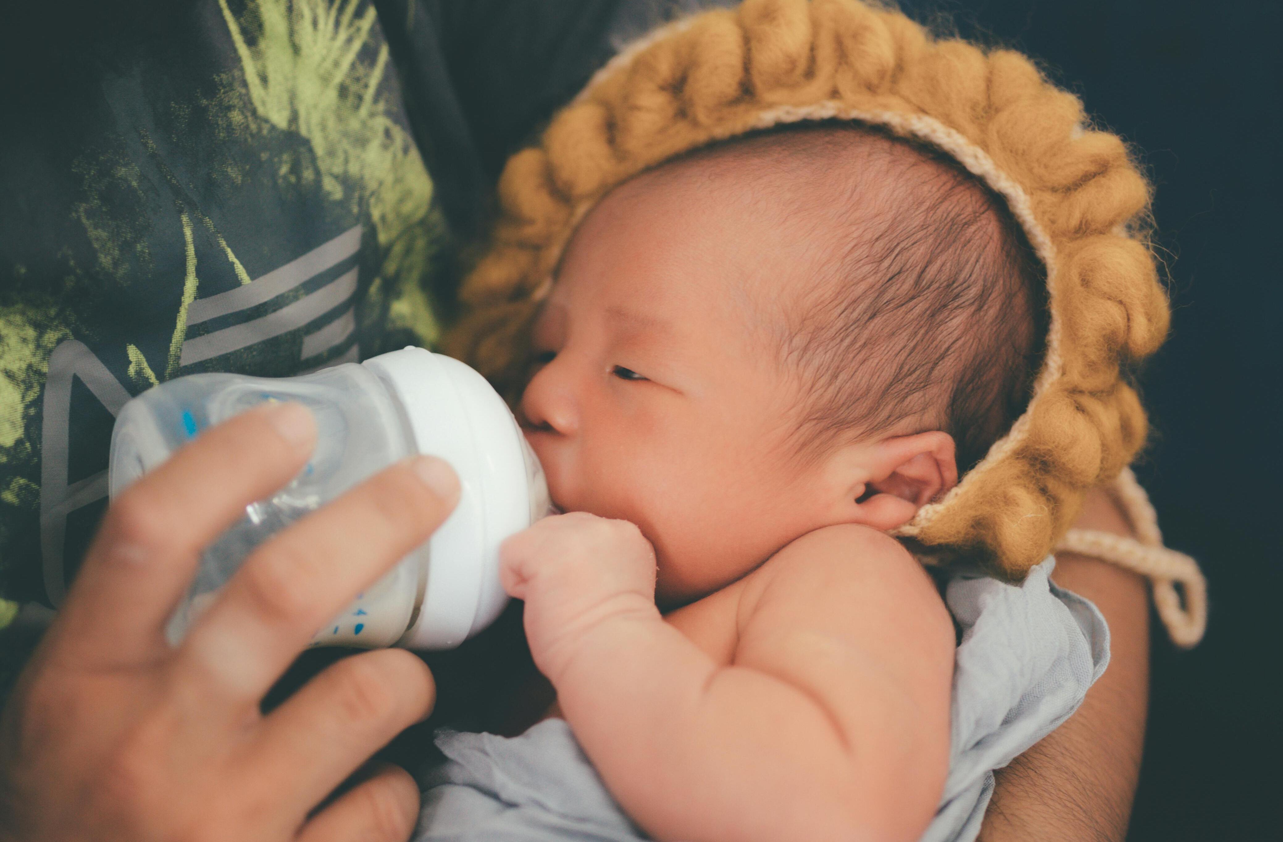 Una persona alimenta a un recién nacido con un biberón mientras el bebé lleva un simpático gorro de león | Fuente: Pexels