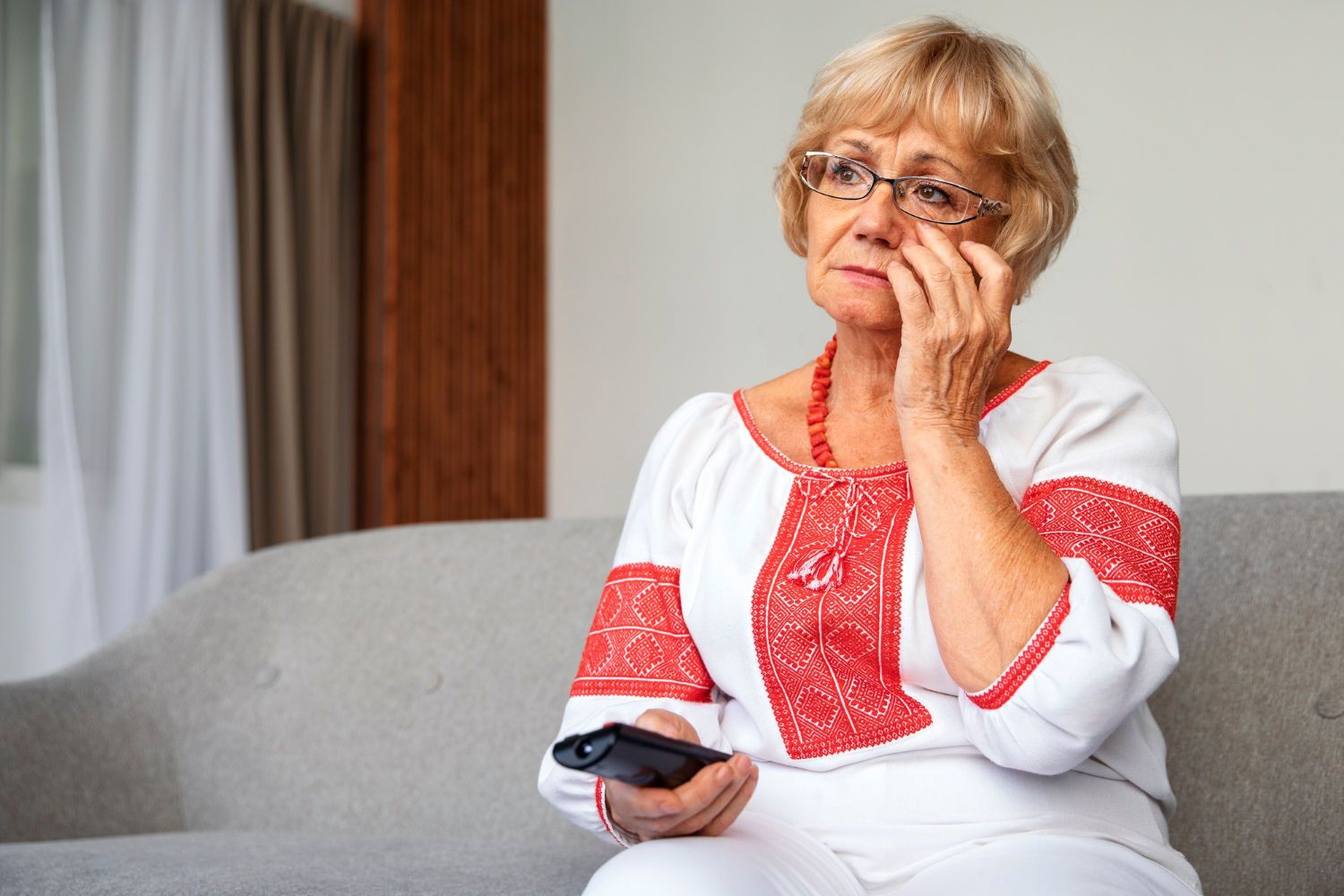 Una anciana triste sujetando el mando de la tele | Fuente: Freepik