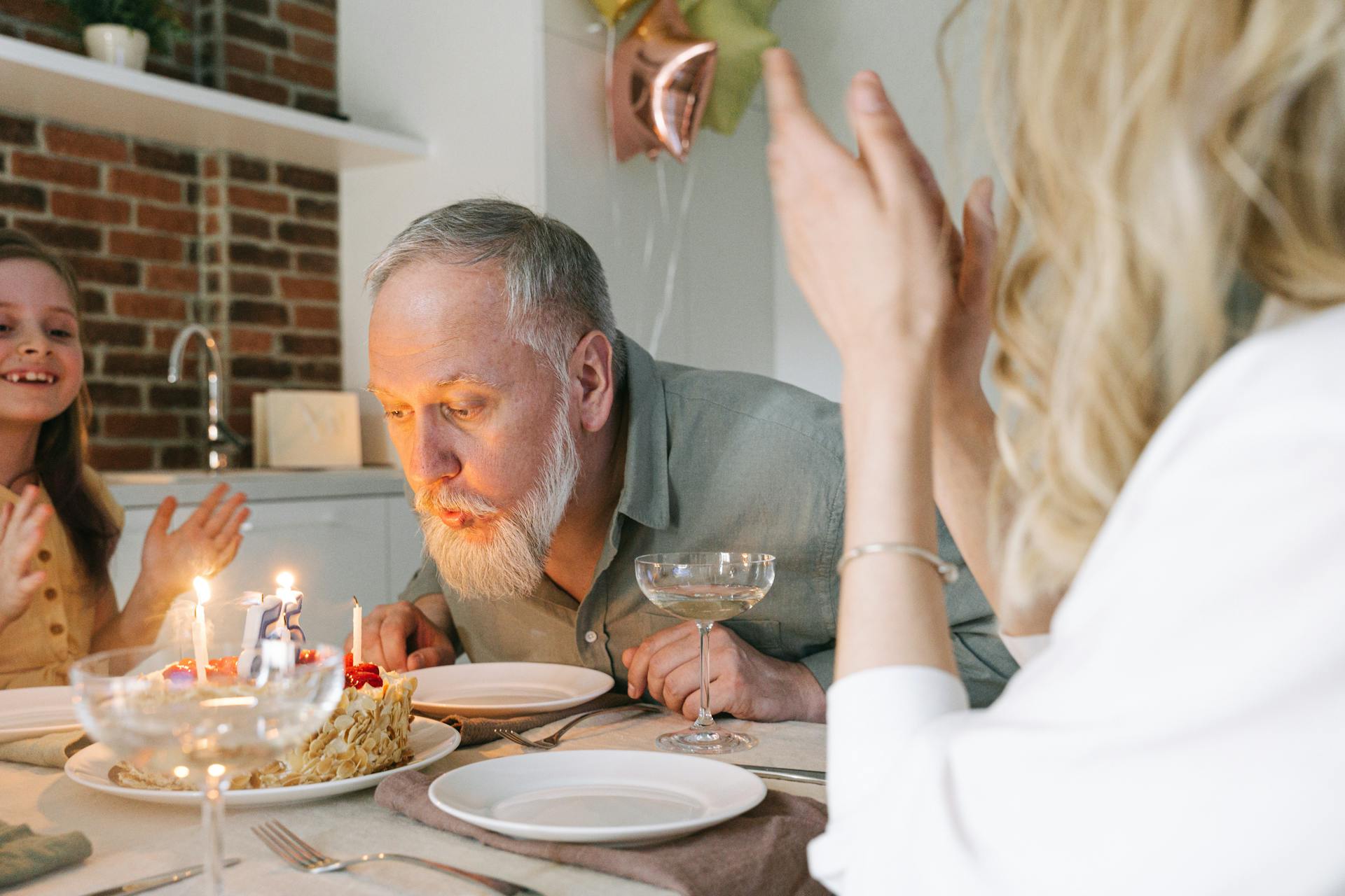 Un hombre sopla las velas de una tarta de cumpleaños con su familia animándole | Fuente: Pexels