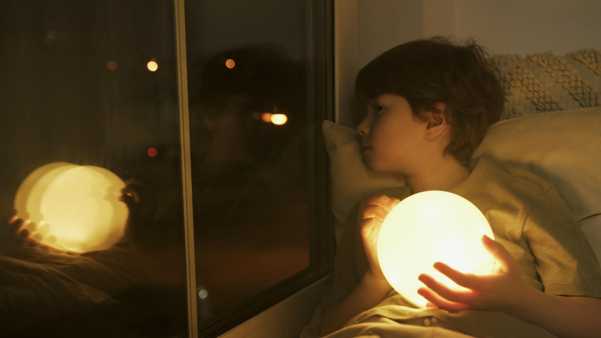 Un niño sosteniendo una bola de luz y mirando por la ventana | Fuente: Pexels