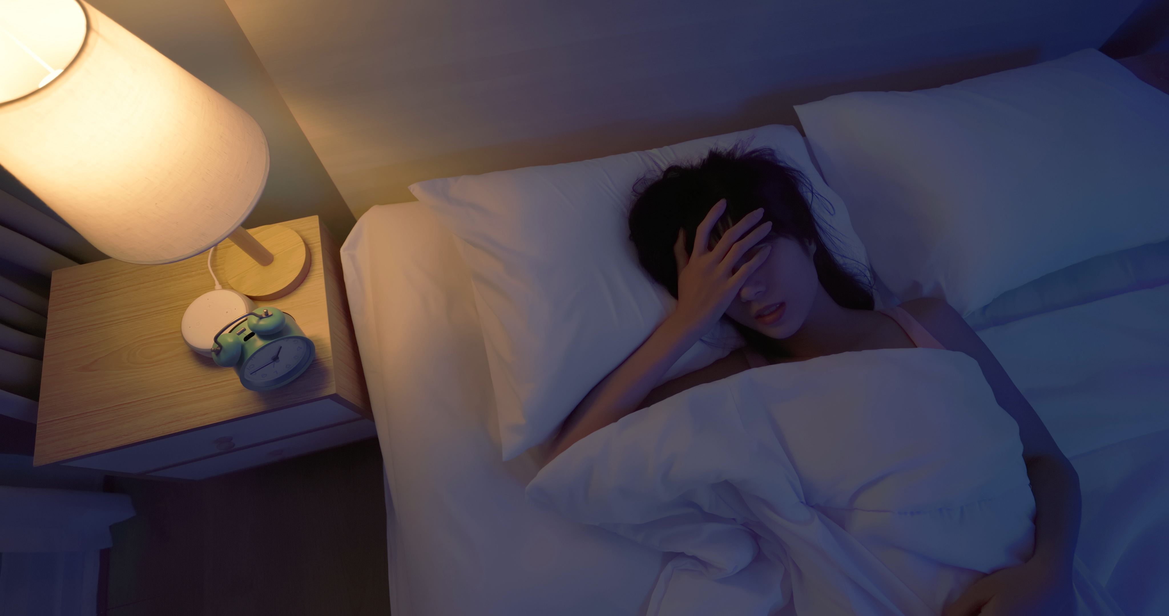 Mujer tumbada en la cama sujetándose la cabeza, aparentemente dolorida | Fuente: Getty Images