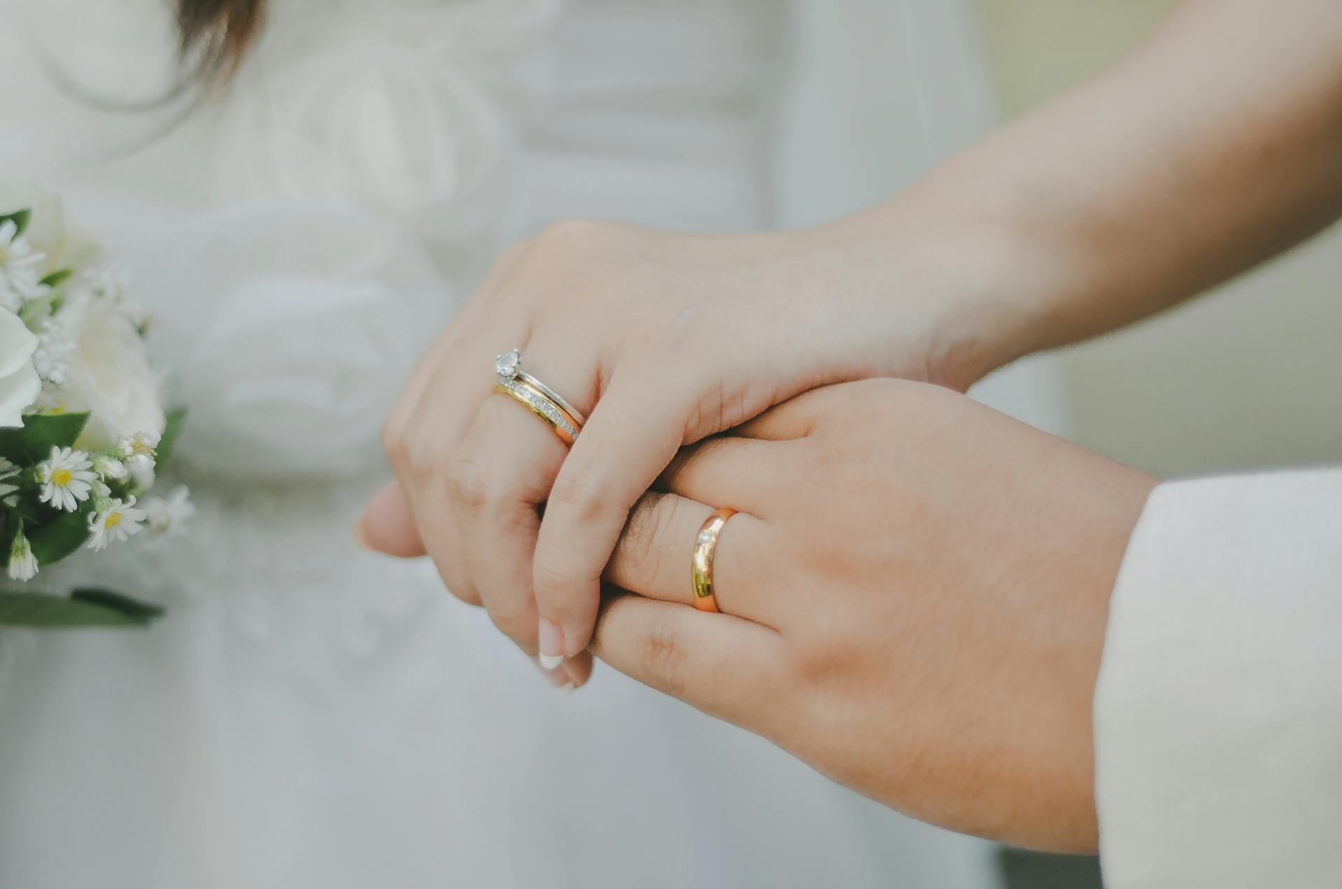 Una novia y un novio tomados de la mano y mostrando sus alianzas | Fuente: Pexels