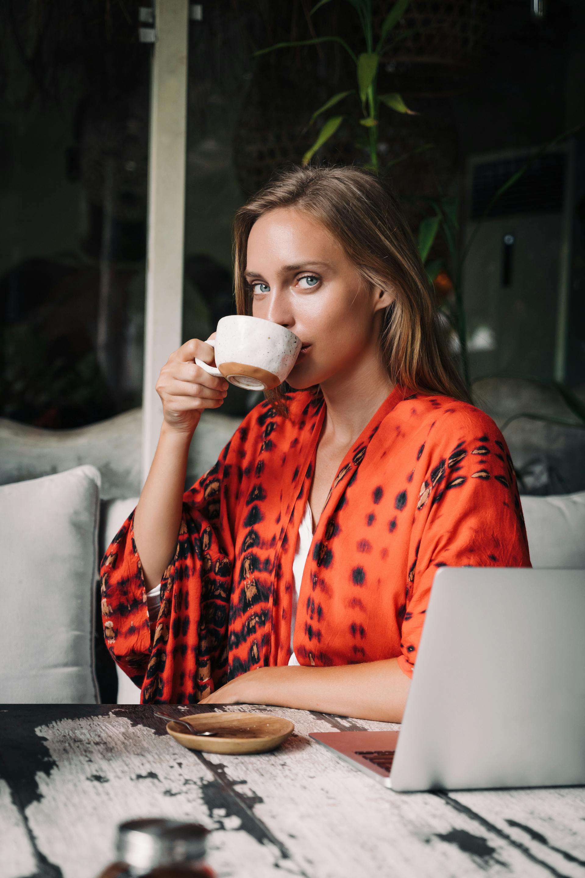 Una mujer tomando café con su portátil delante | Fuente: Pexels