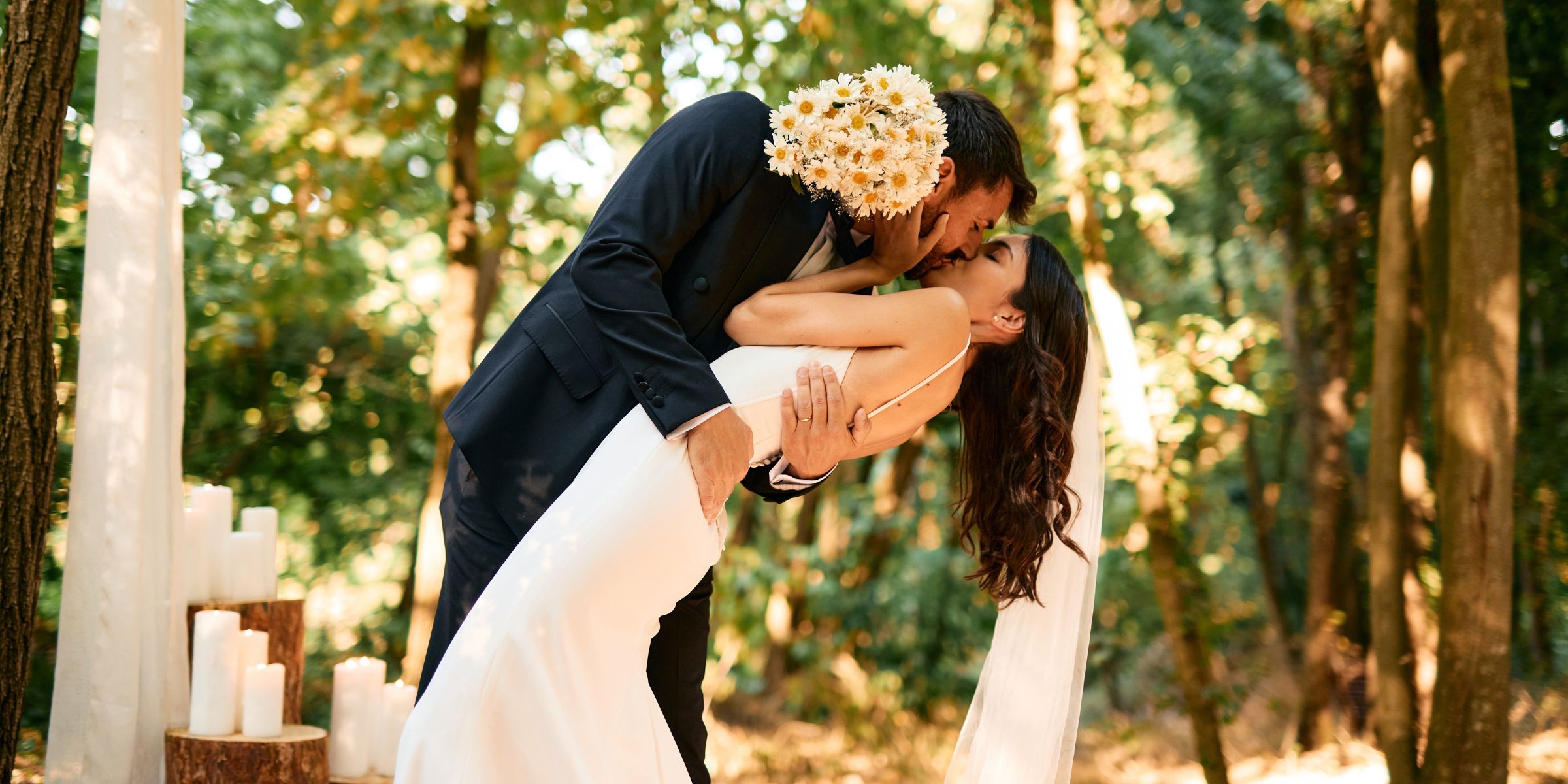 Groom holding a bouquet, bending the bride over for a kiss during a romantic forest wedding ceremony | Source: Getty Images
