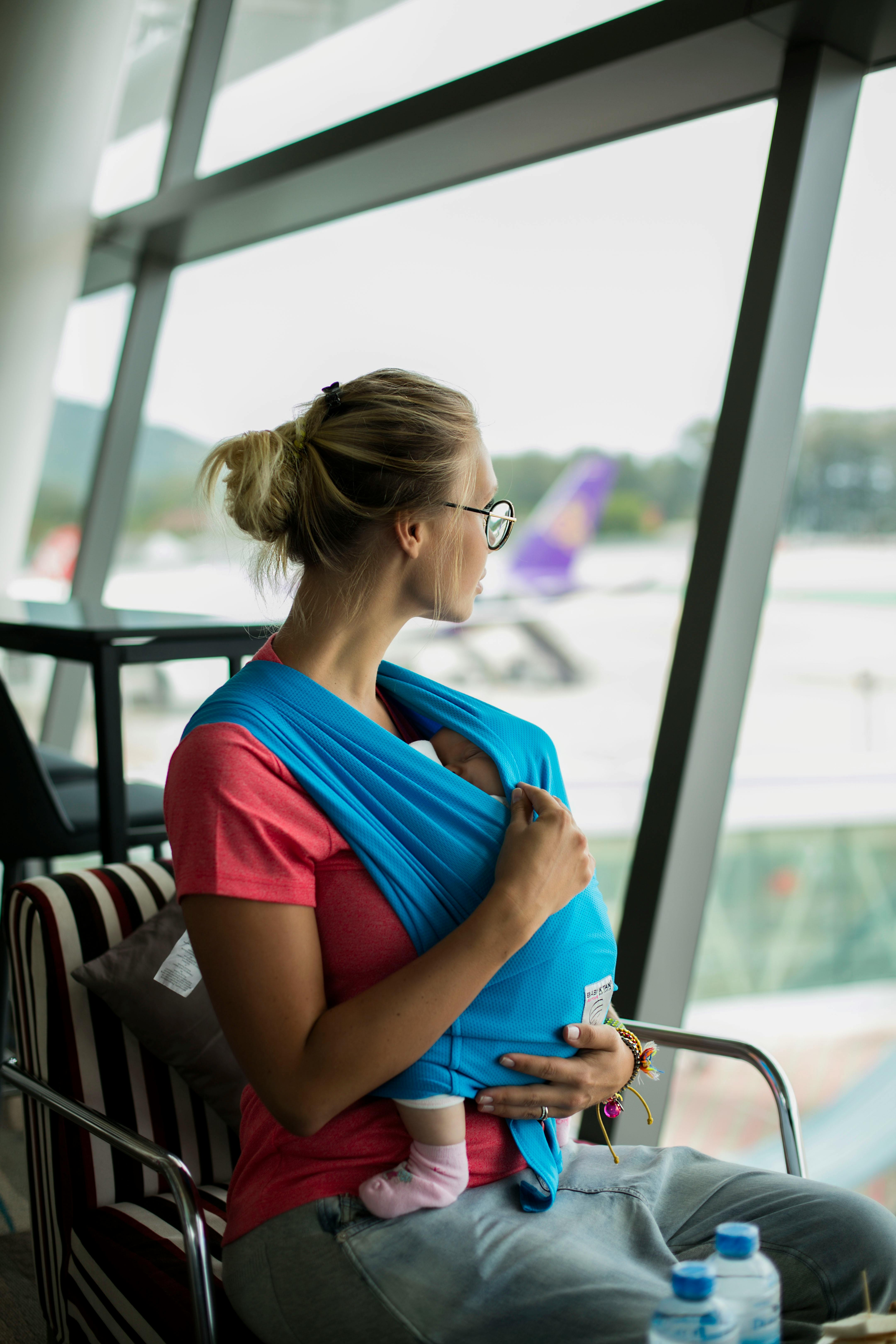 Mujer rubia con un bebé mirando por la ventanilla de un aeropuerto | Fuente: Pexels