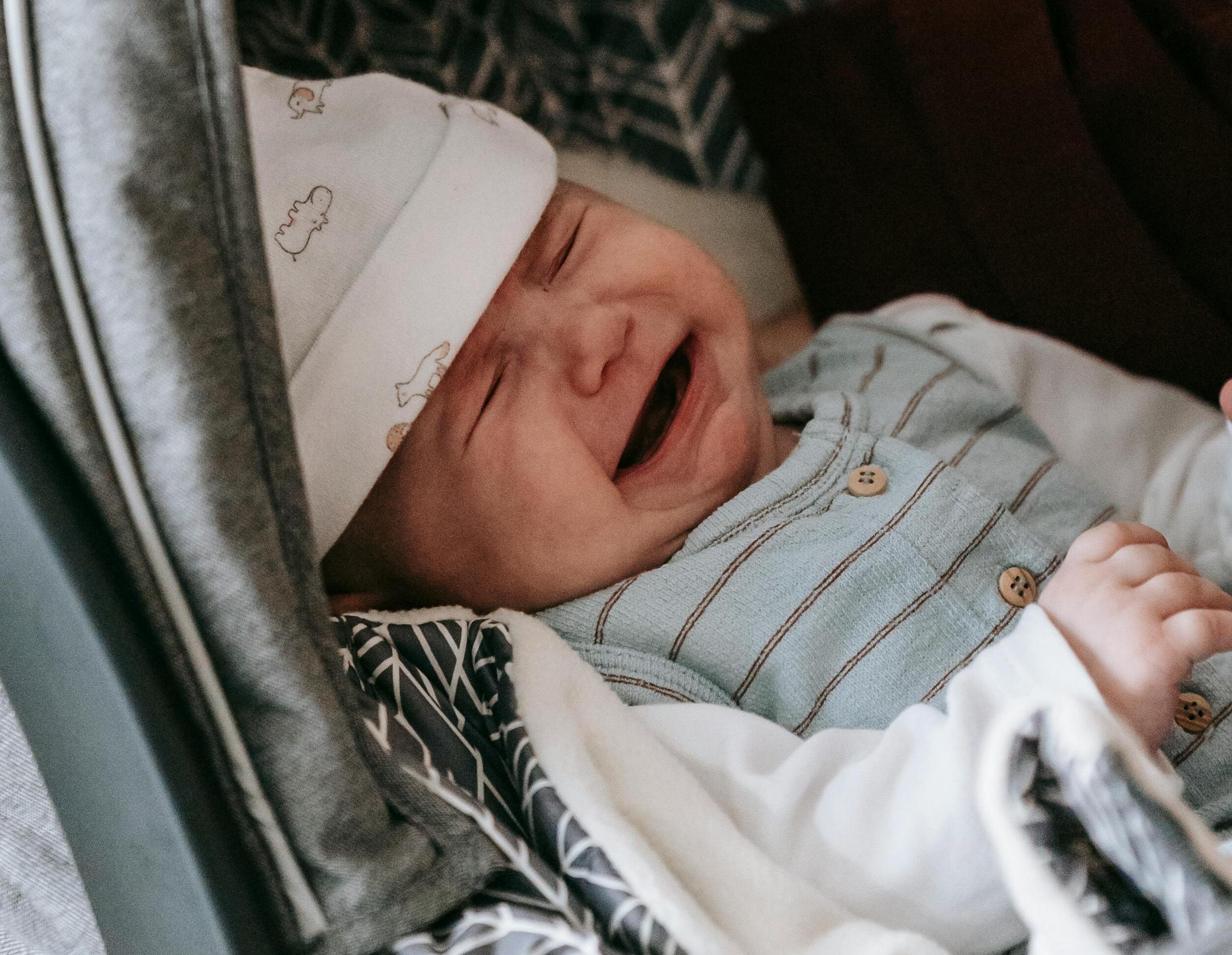 Un bebé con un body a rayas y un gorrito blanco, llorando | Fuente: Pexels