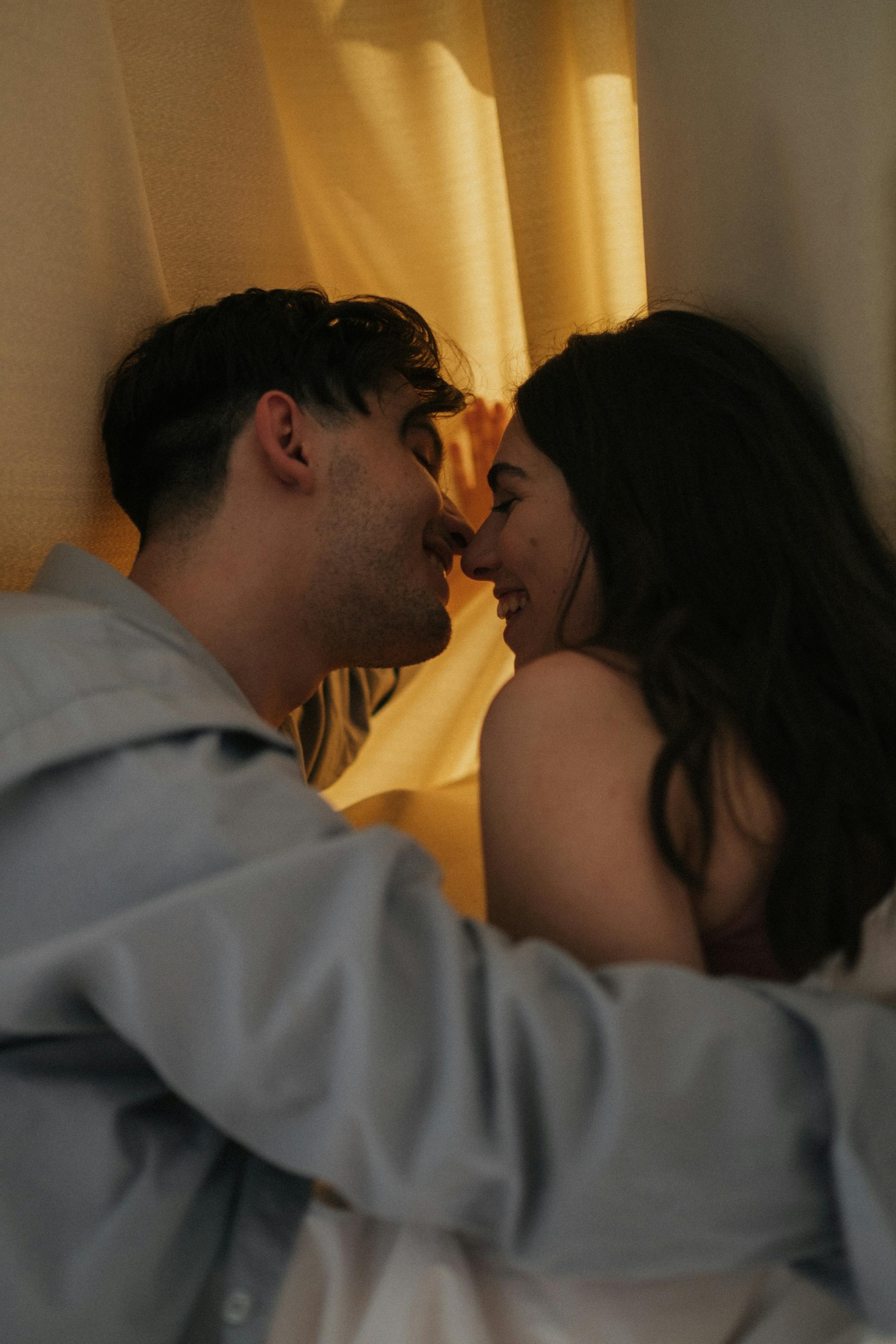 Una pareja feliz besándose detrás de una cortina | Fuente: Pexels